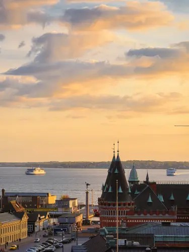 Sunset over Helsingborg waterfront cityscape with historic red clock tower and ferry in the distance.