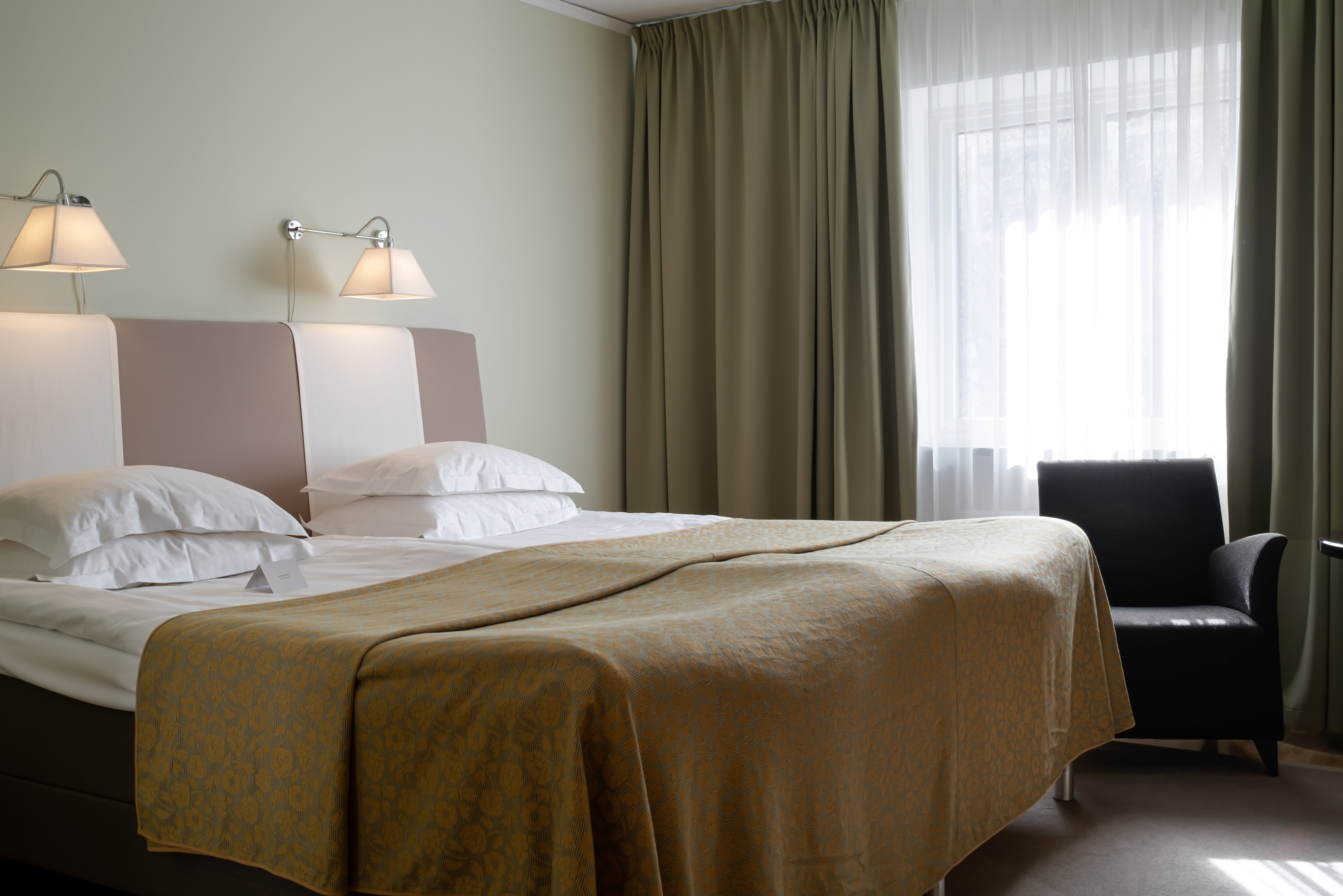 Hotellrum med säng, fåtölj och gardiner