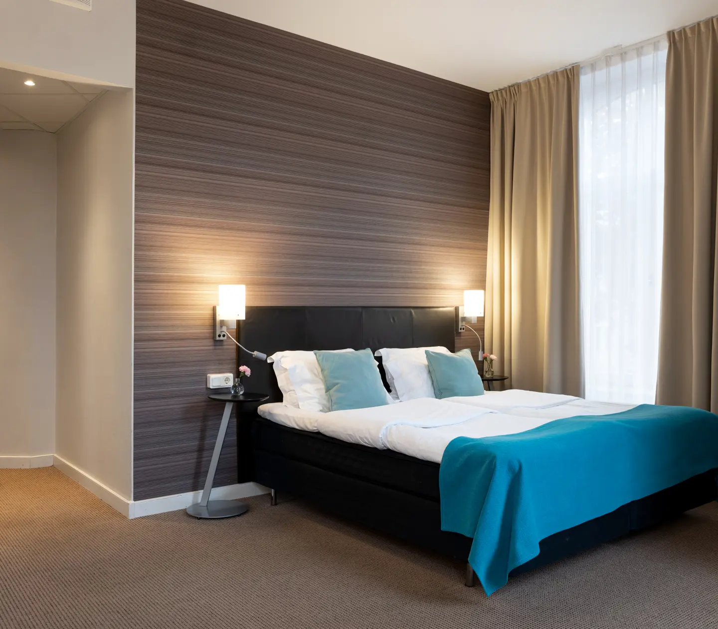 Comfortable hotel room with double bed, warm textiles and large windows