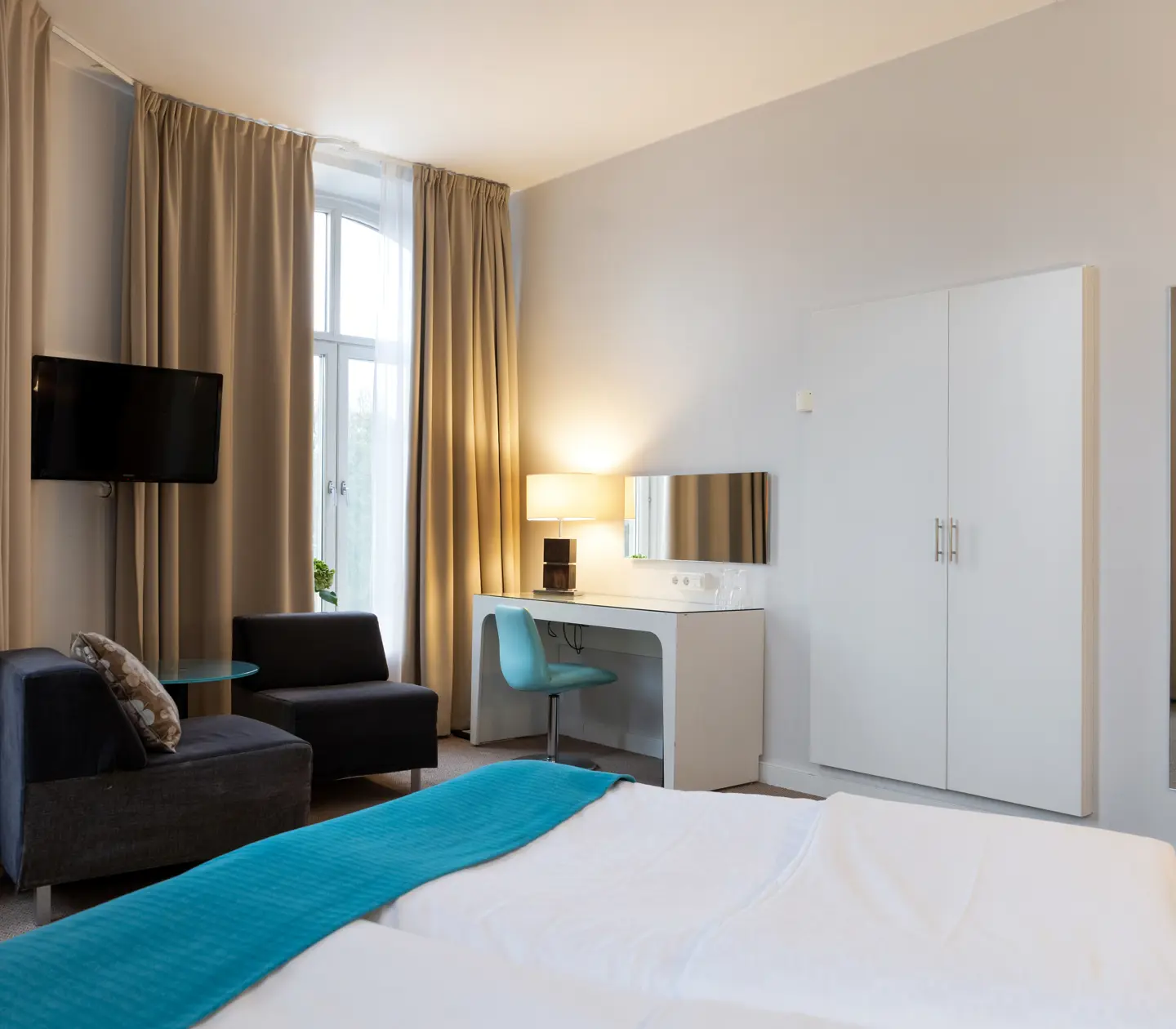Bright hotel room with bed, desk and armchairs