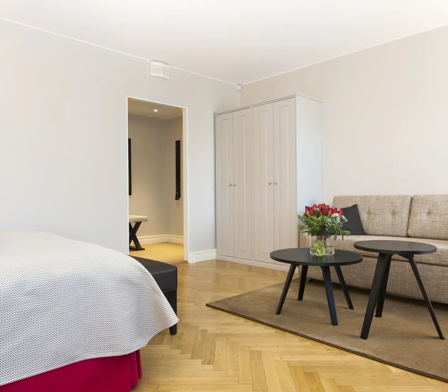 Bright hotel room with sofa, wardrobe and bouquet of roses