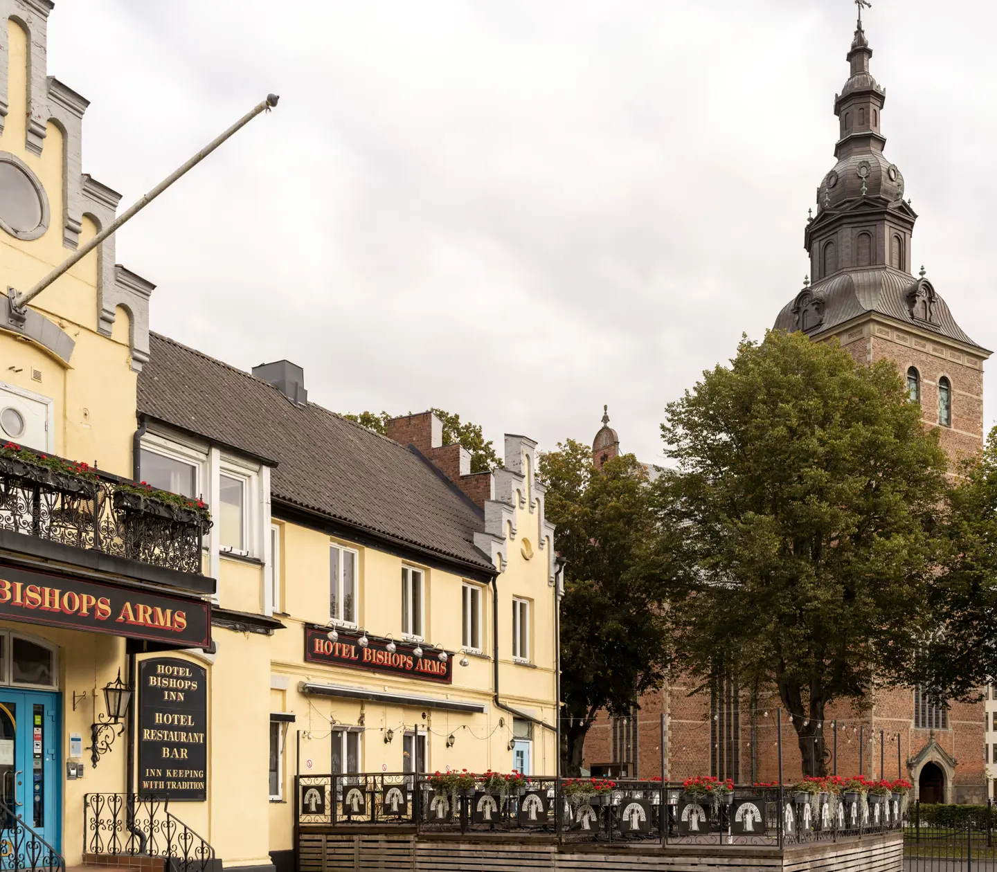 The yellow facade of the Hotel Bishops Arms with church behind and outdoor dining in front