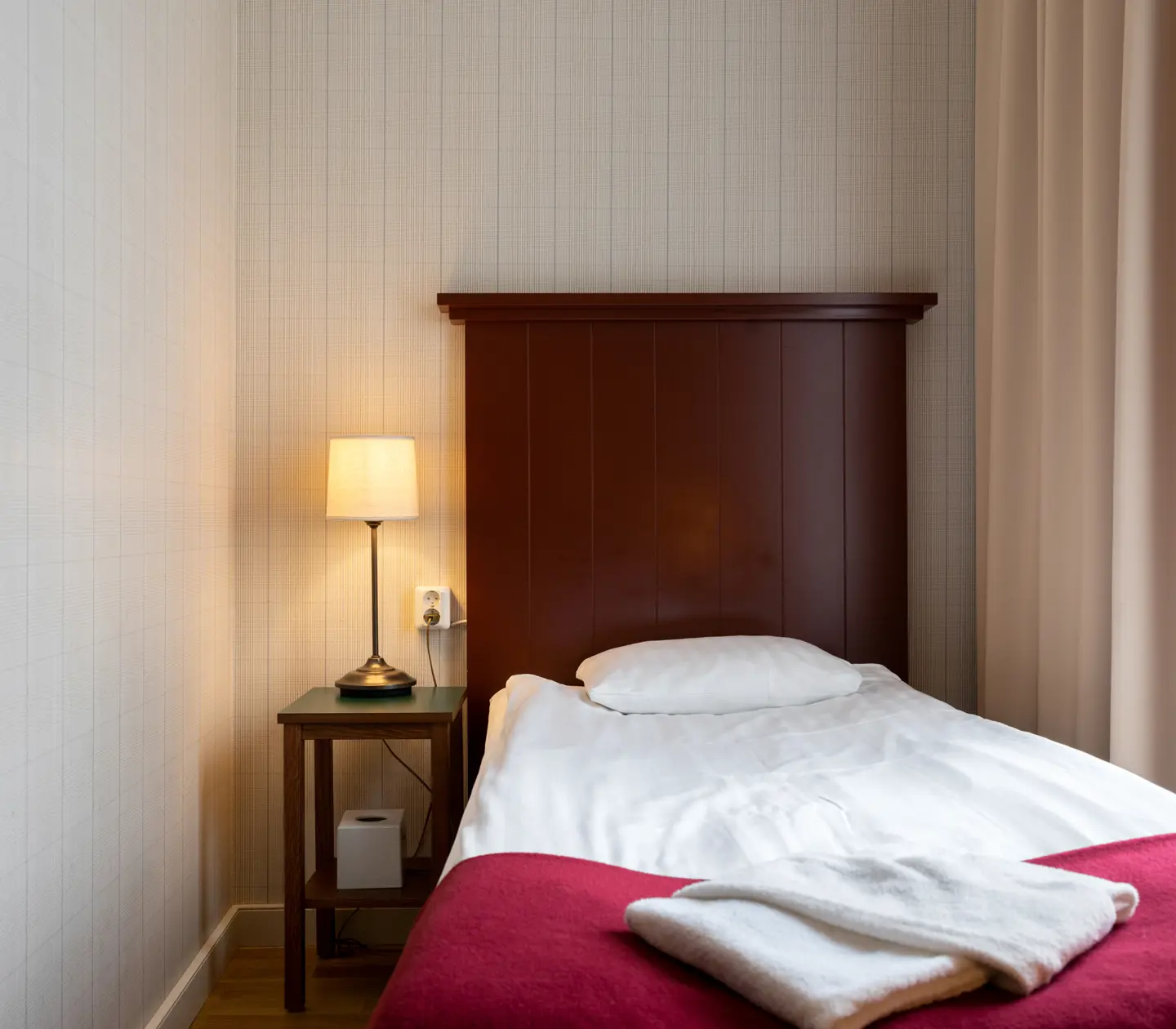 Cozy hotel room with bed, wooden headboard and bedside lamp