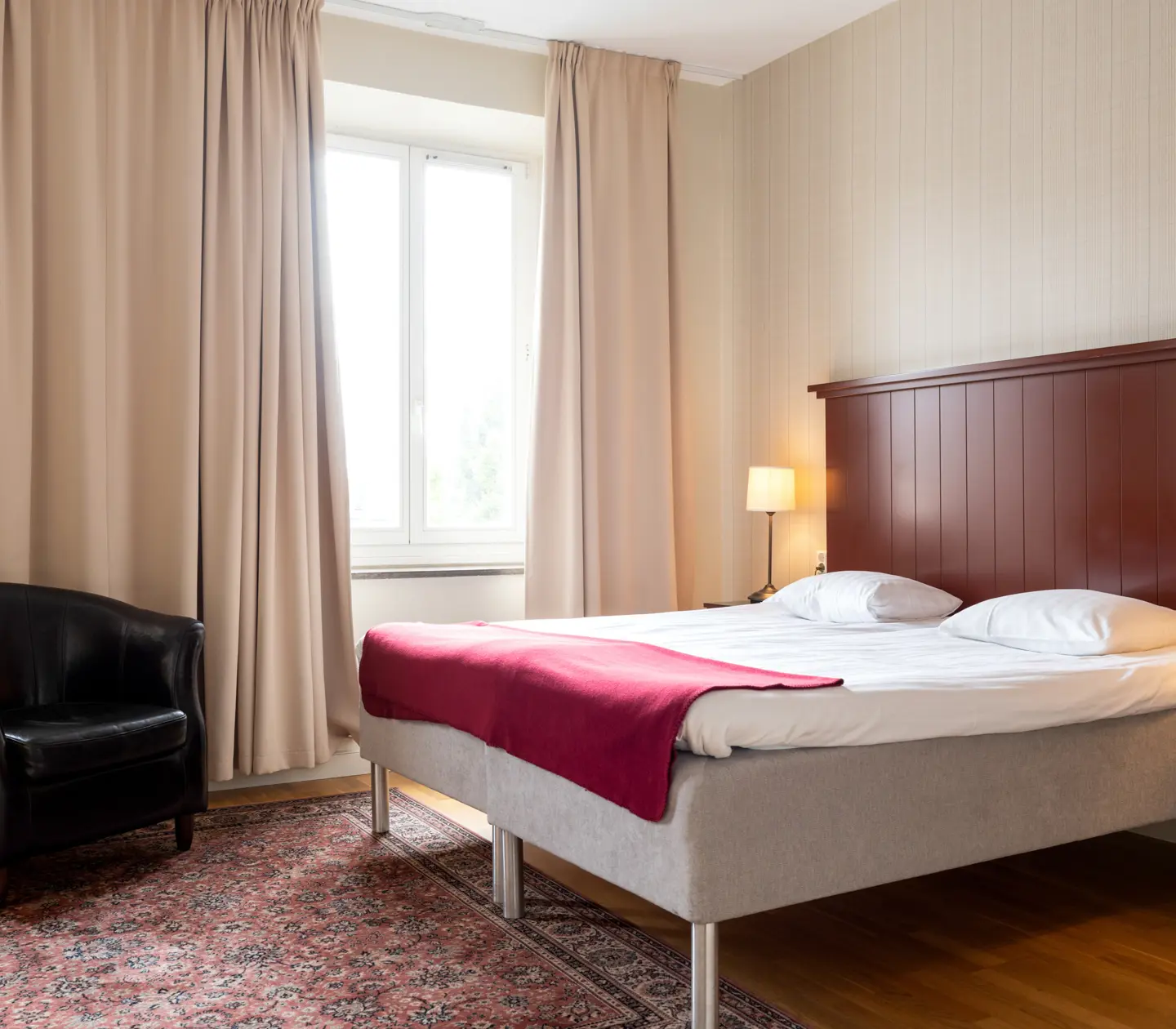 Cozy hotel room with bed, wooden headboard and black leather armchair