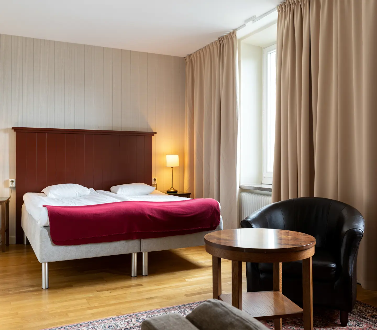 Cozy hotel room with bed, wooden headboard and black leather armchair