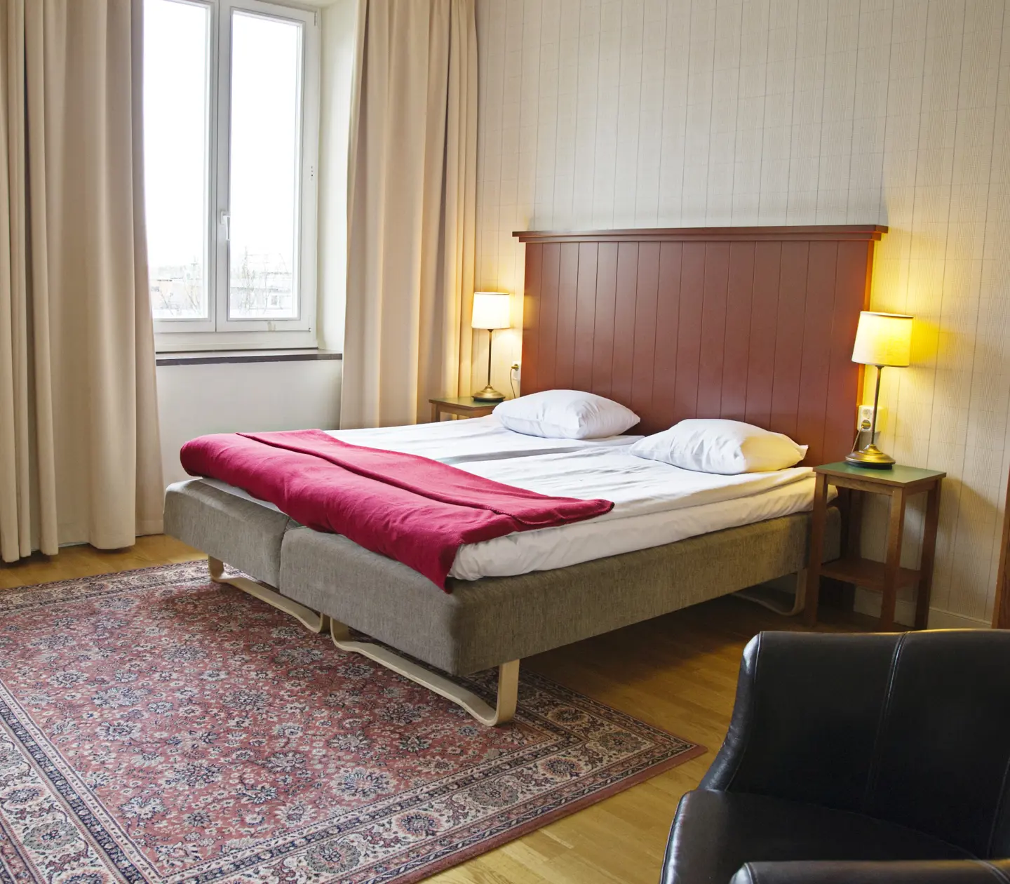 Cozy hotel room with bed, wooden headboard and black leather armchair