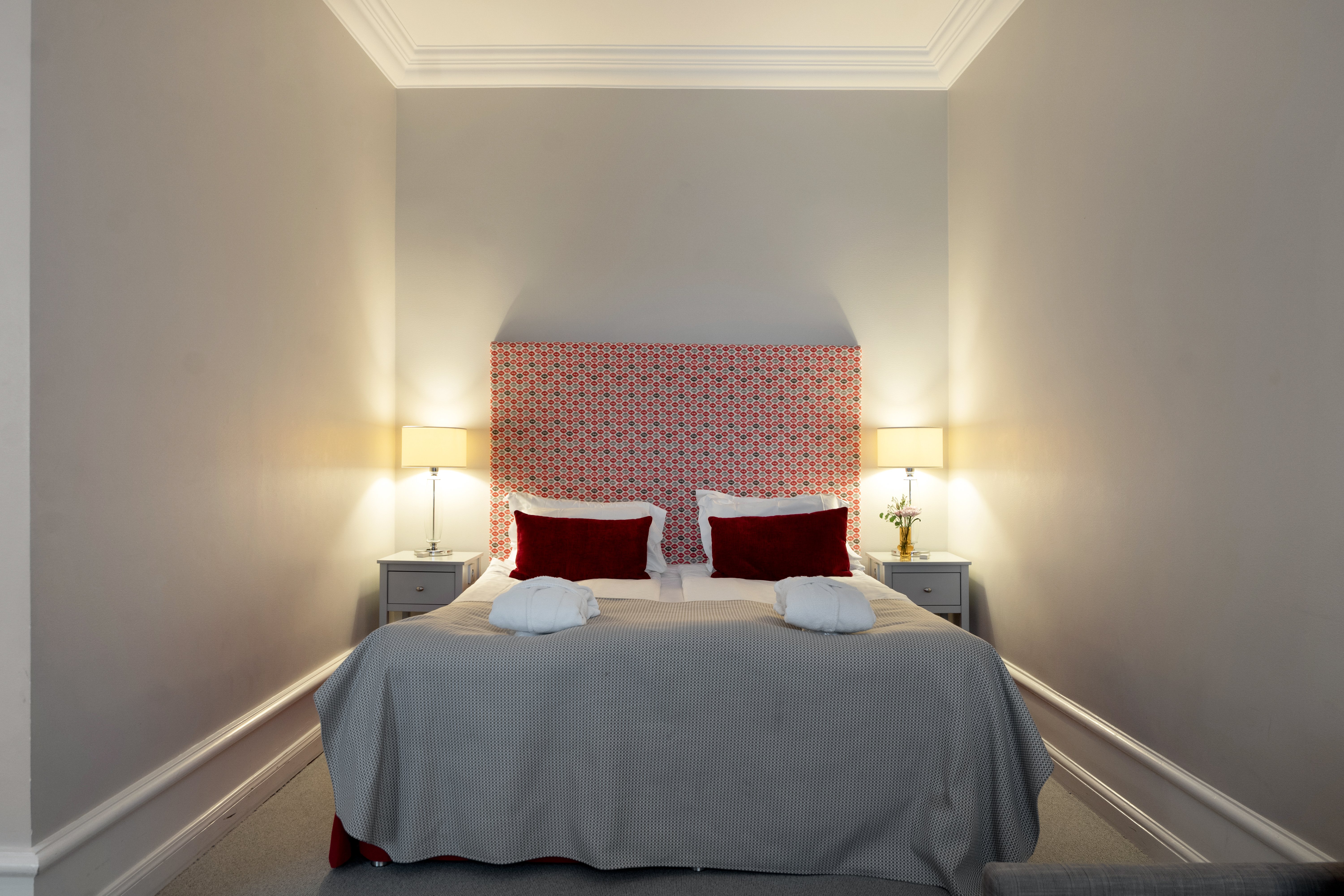 Hotellrum med dubbelsäng, röd sänggavel och sänglampor