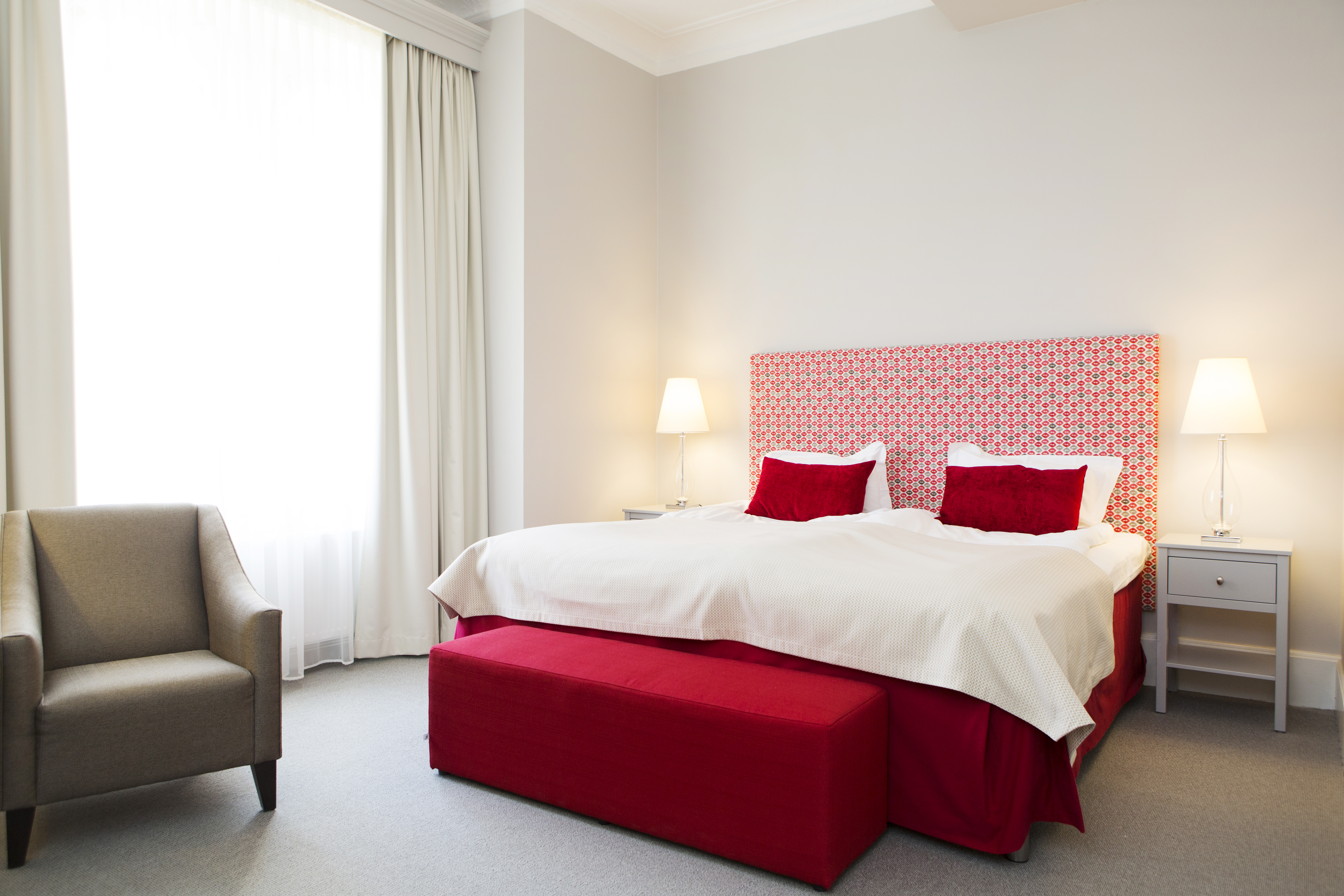 Ljust hotellrum med säng, röd sänggavel och fåtölj