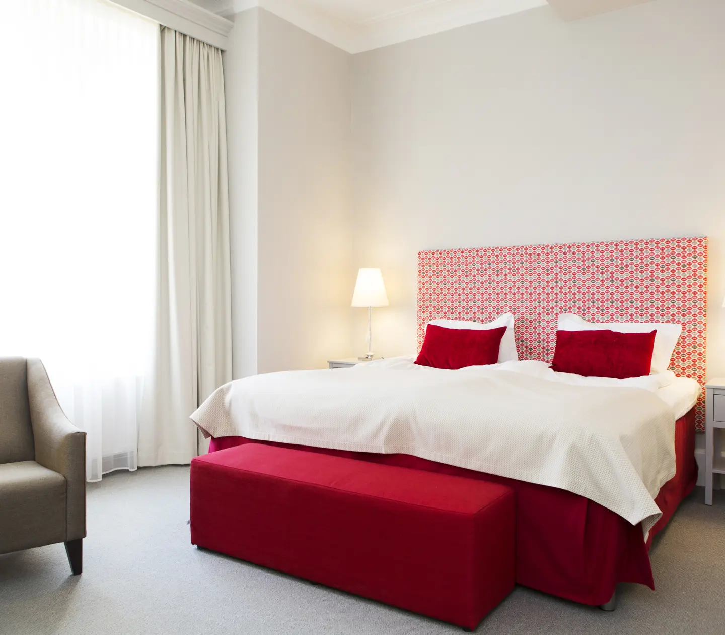 Bright hotel room with bed, red headboard and armchair