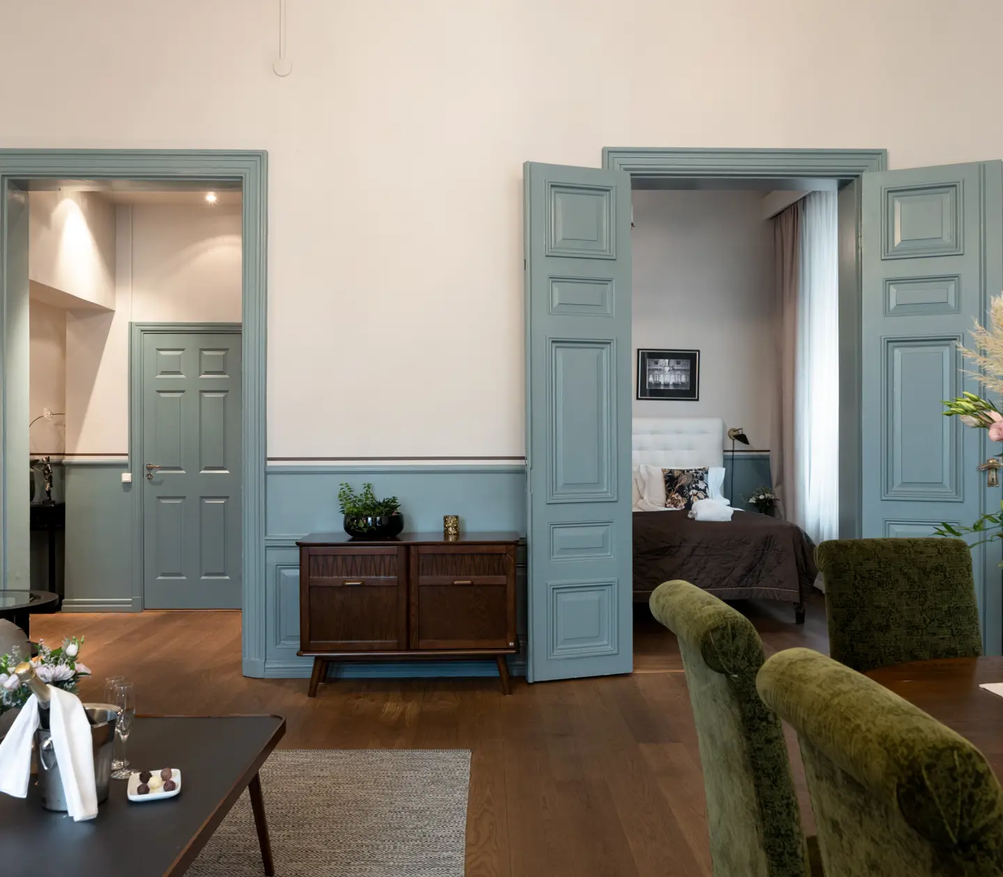 Bright suite with dining table, dresser and green doors to bedroom