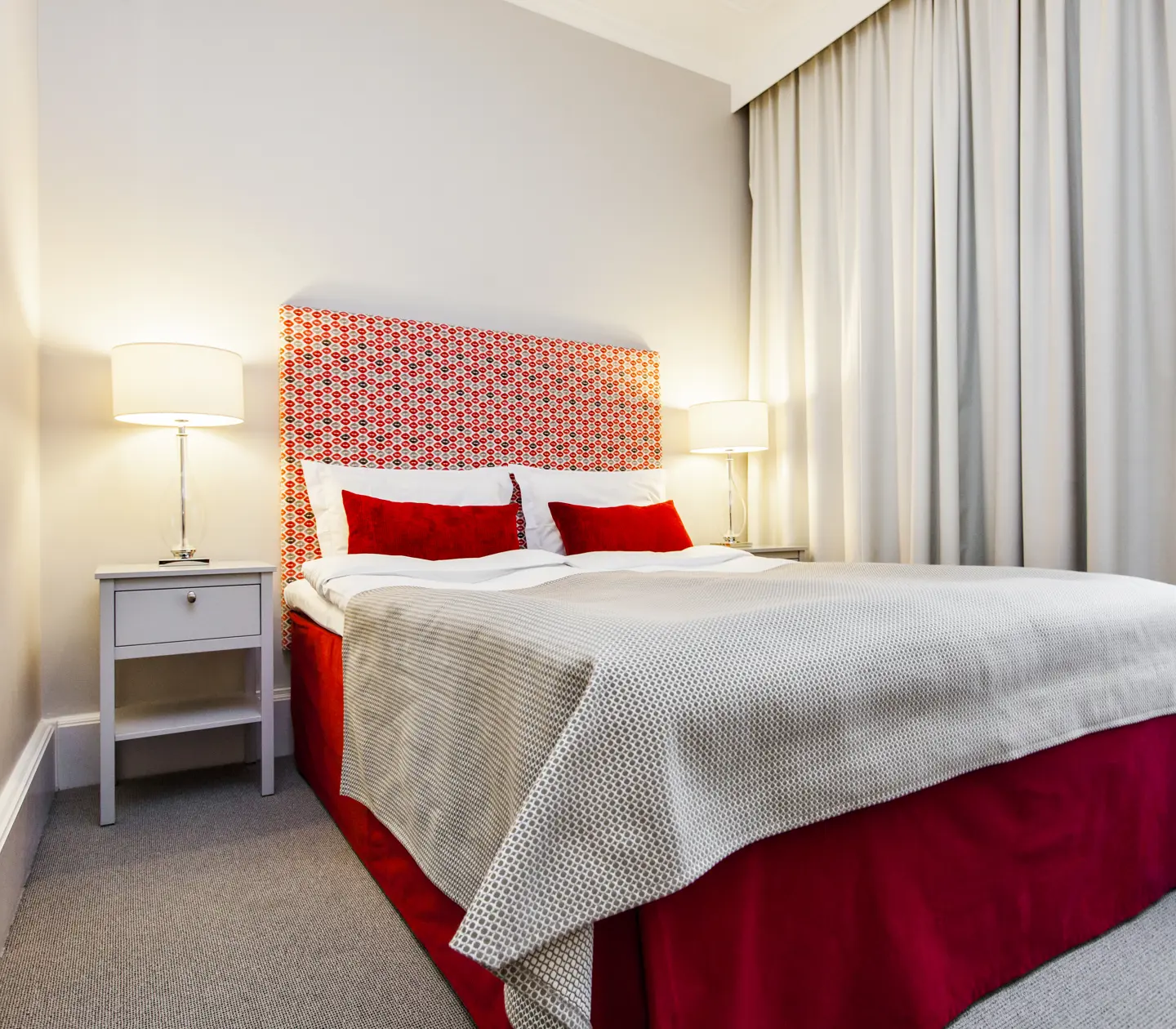 Bright hotel room with single bed, red headboard and bedside lamps