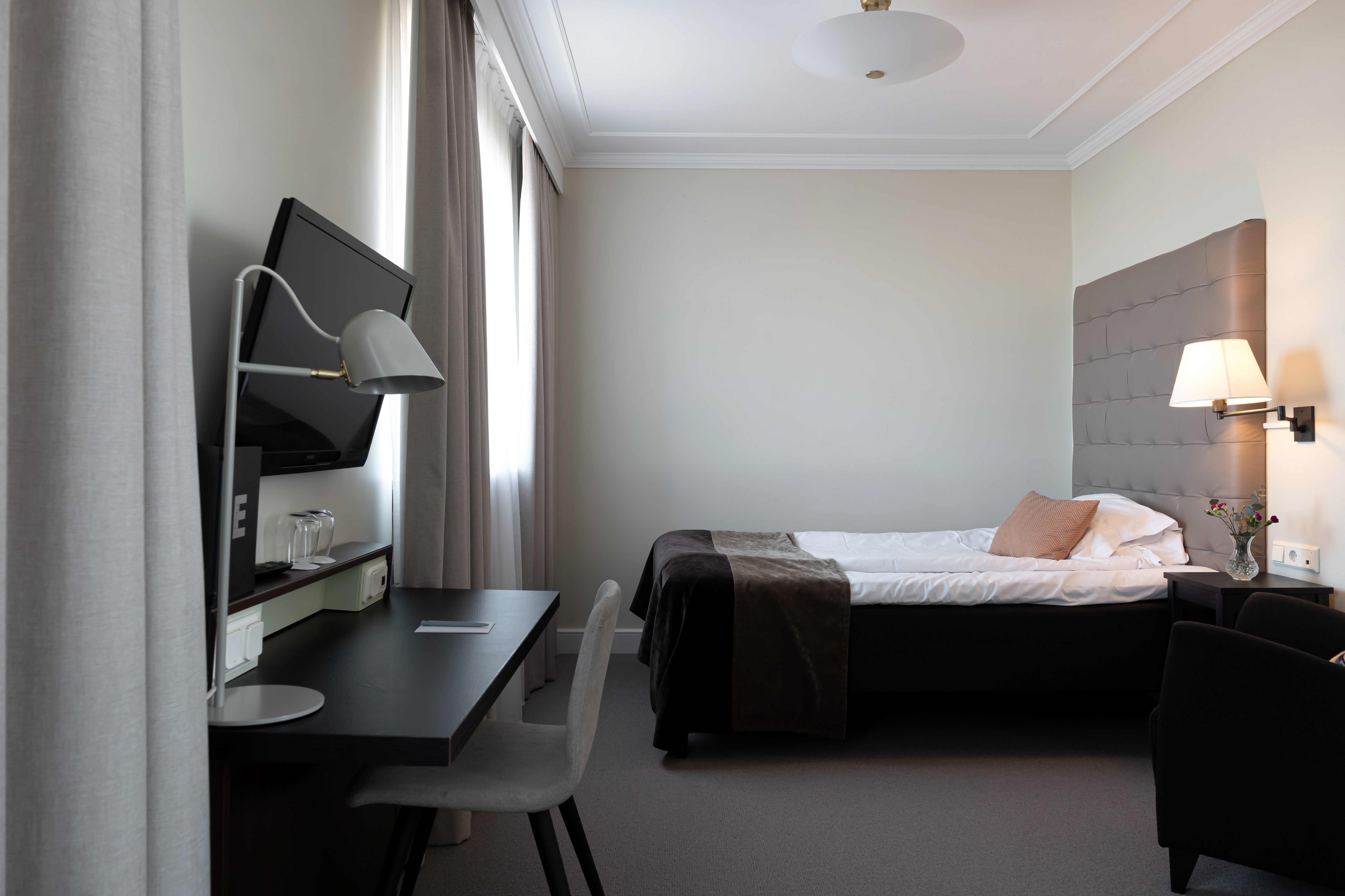 Ljust hotellrum med skrivbord, säng och sänglampa