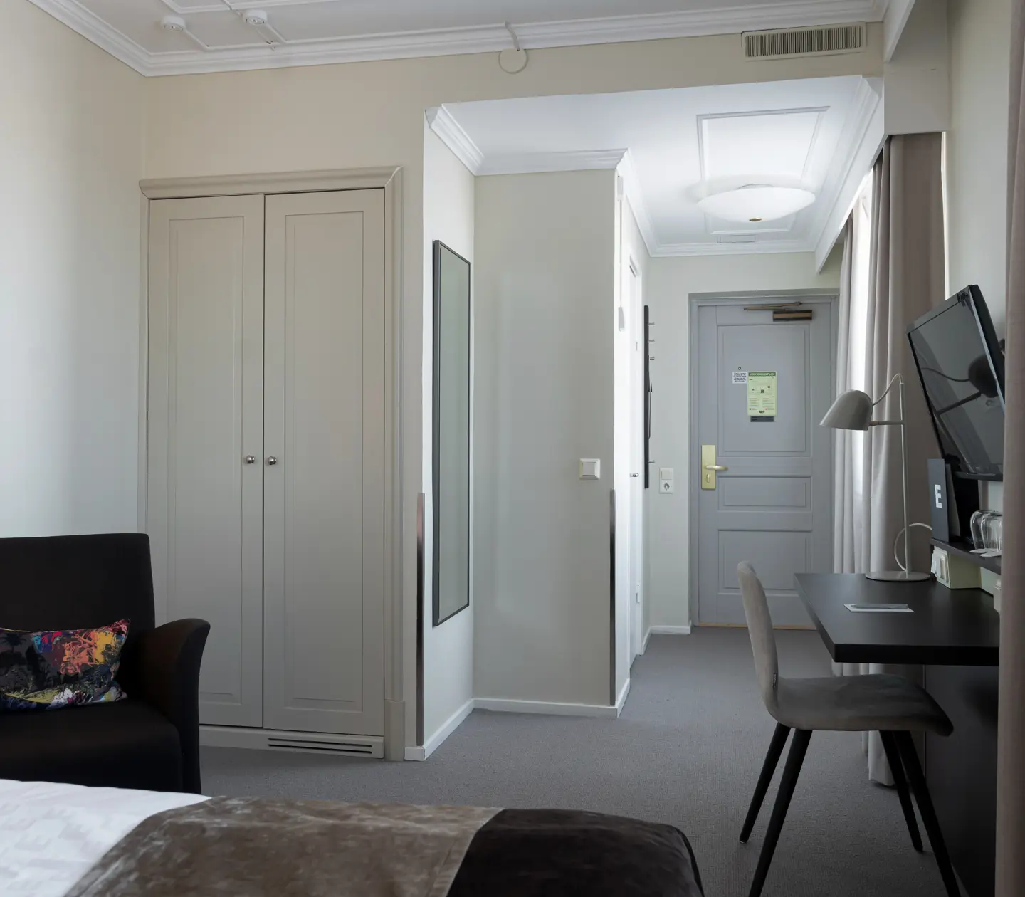 Bright hotel room with desk, wardrobe and armchair
