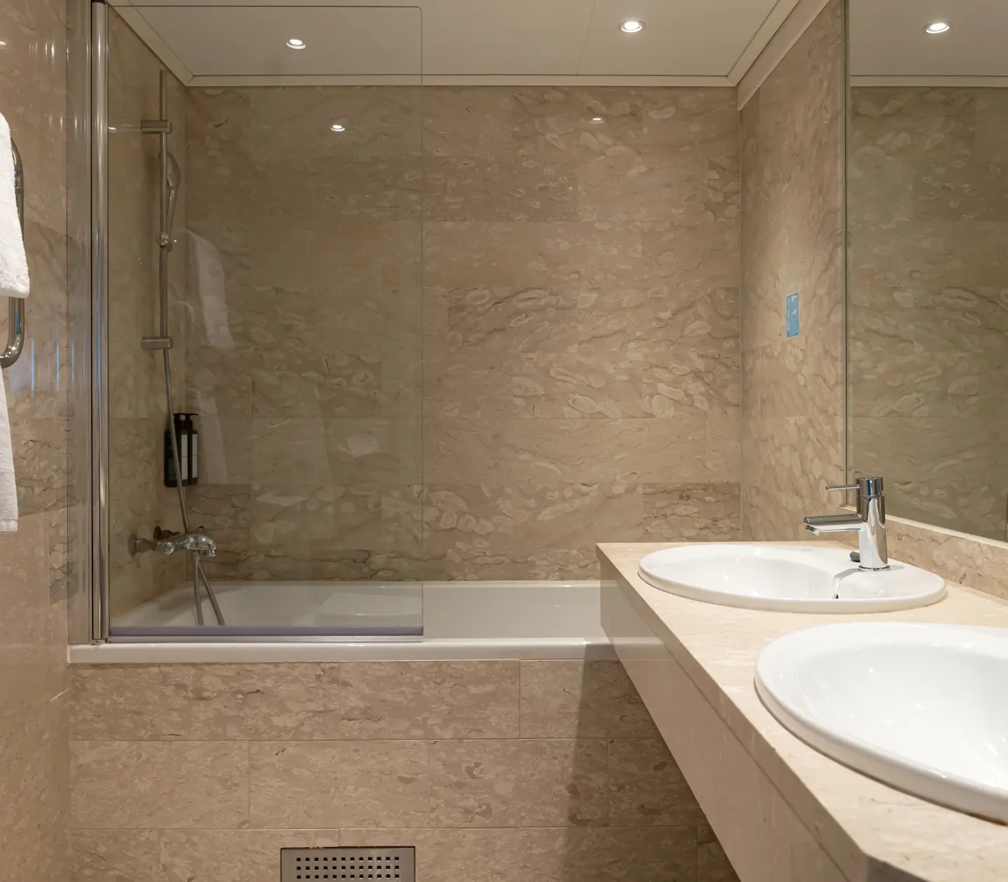 Beige bathroom with double sinks, bathtub and mirror