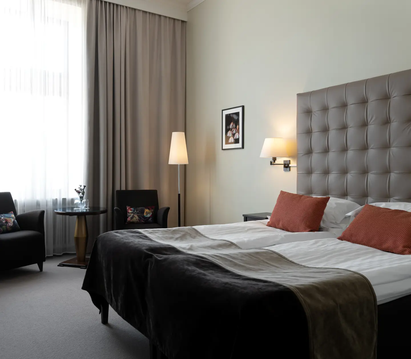Bright hotel room with bed, large headboard and armchairs