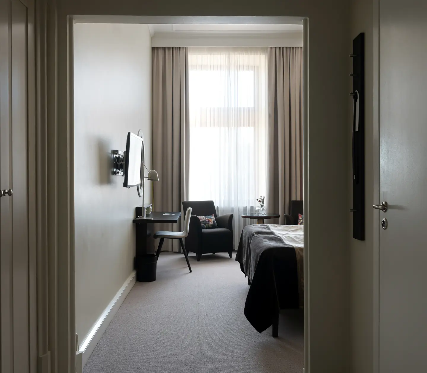 Bright hotel room with desk, wardrobe and armchair