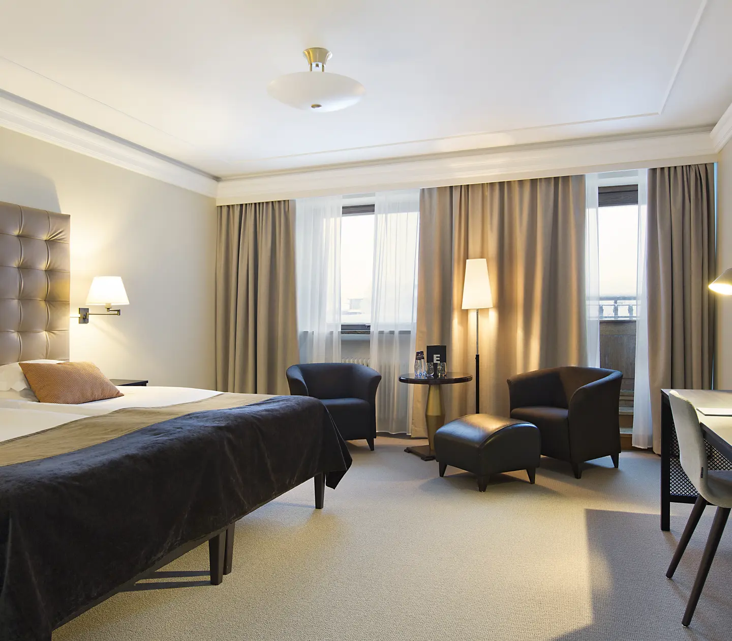 Bright hotel room with bed, armchairs and desk