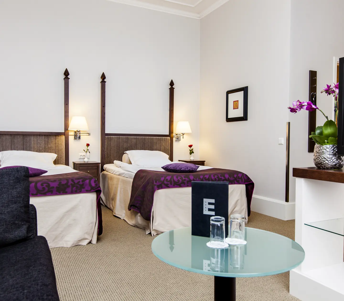 Bright hotel room with two beds, bedside table and TV