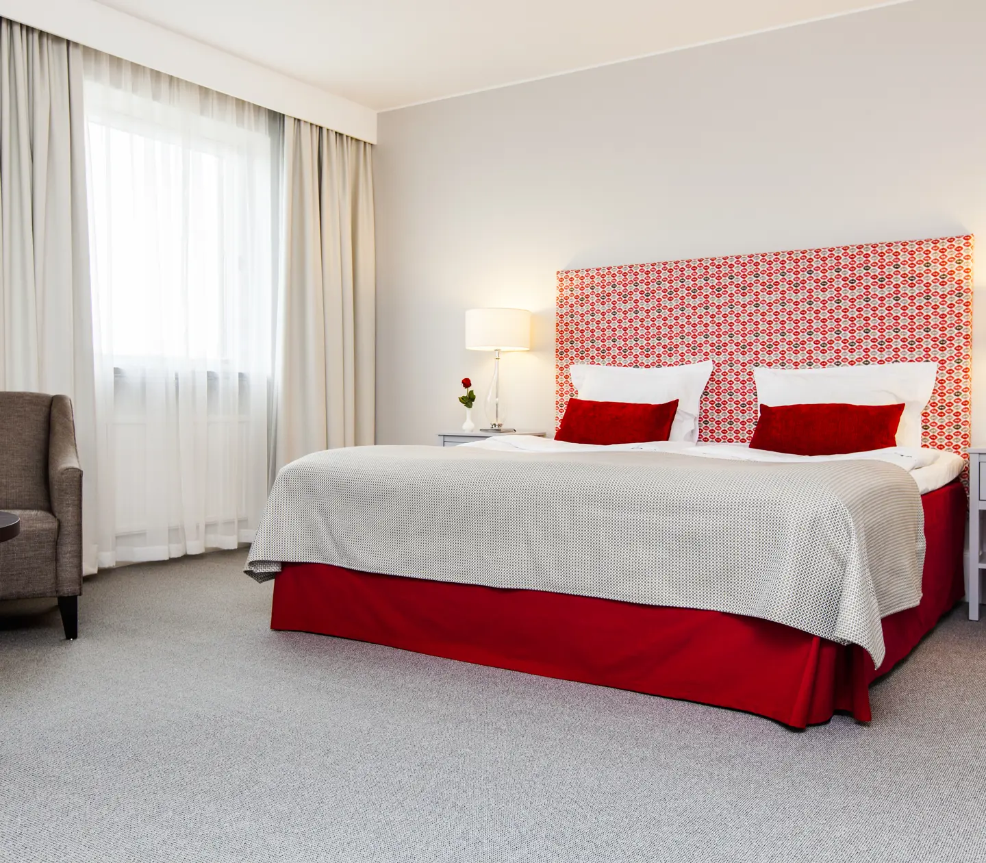 Bright hotel room with bed, red headboard and armchair