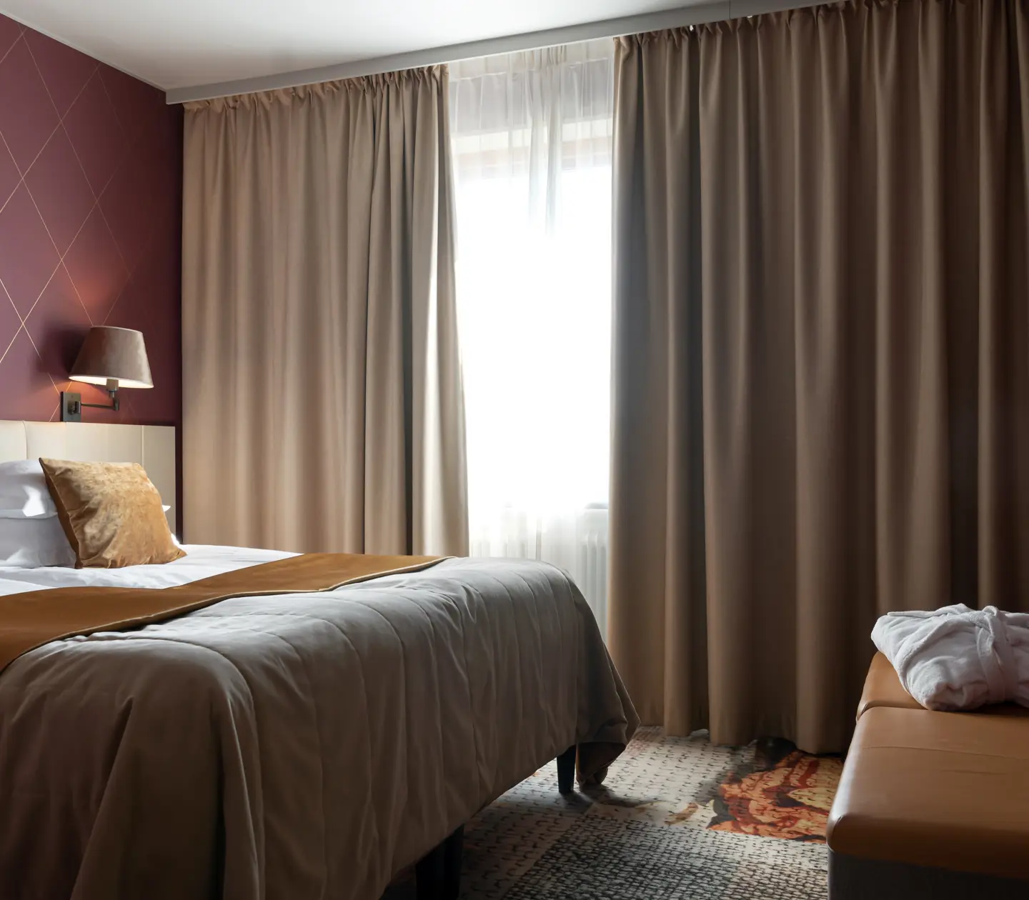 Suite with double bed, window and burgundy wallpaper