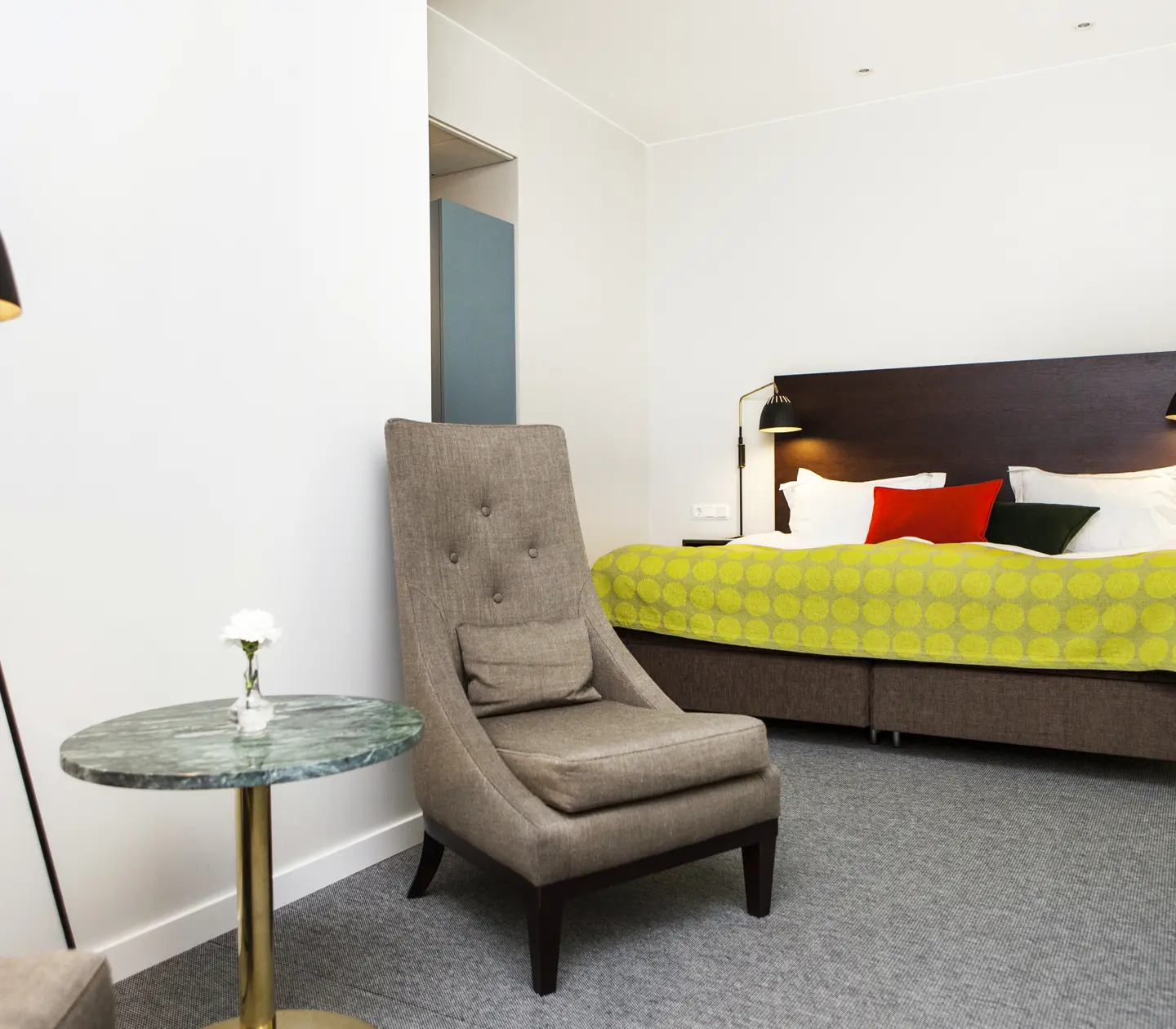 Bright hotel room with bed, armchair and lamp