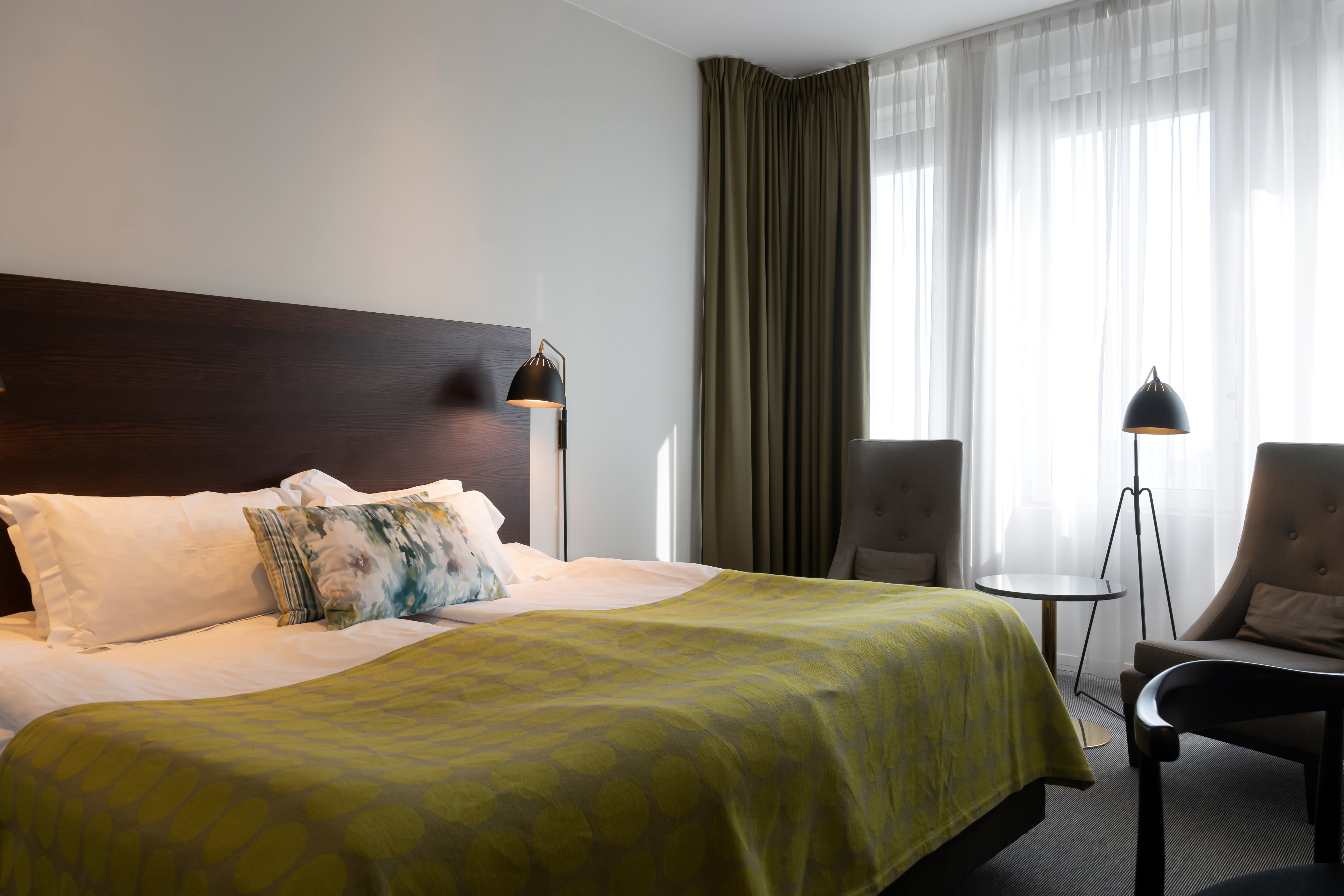 Bright hotel room with bed, armchairs and window