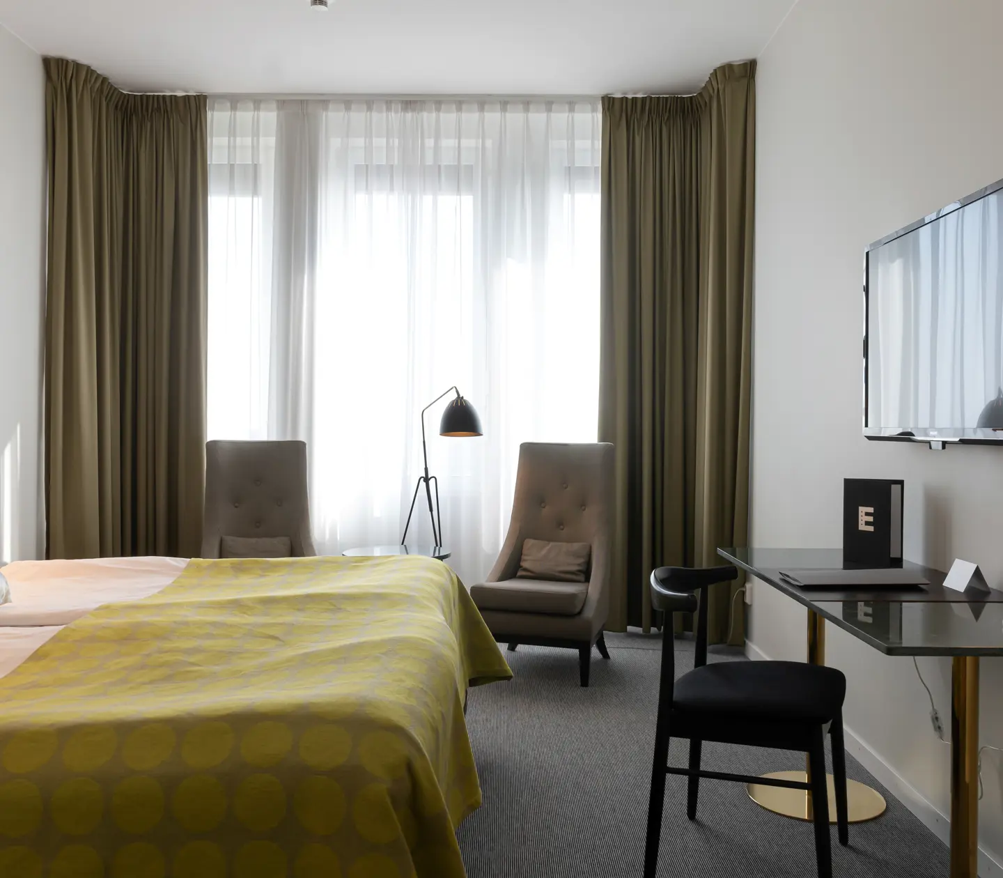 Bright hotel room with bed, armchair and desk