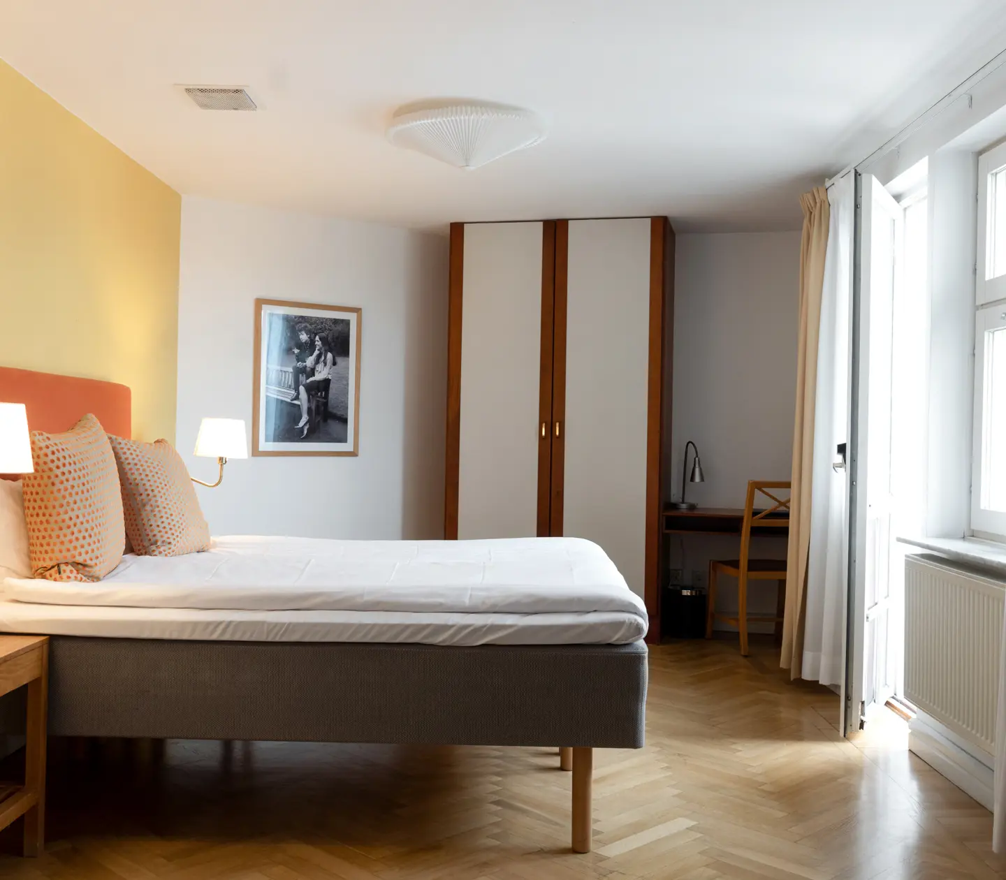 Bright hotel room with bed, wardrobe and bedside lamps