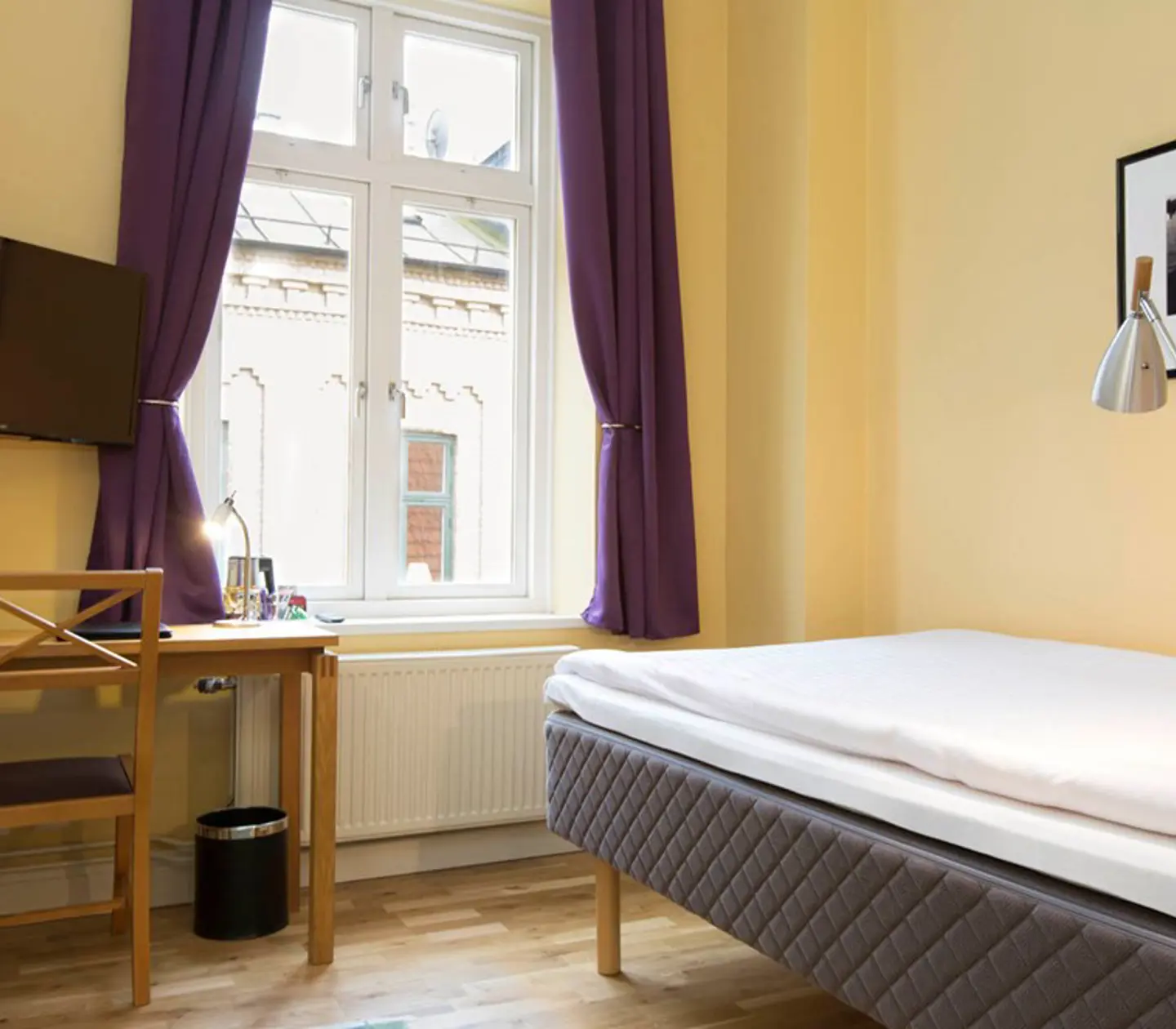 Yellow hotel room with bed, desk and window
