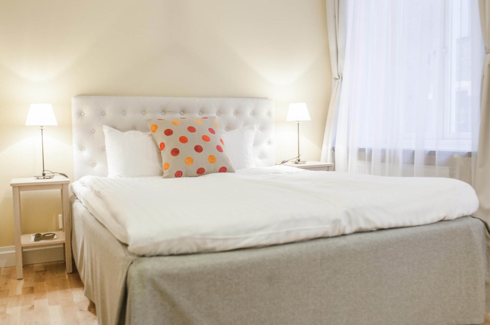 Hotellrum med säng, vit sänggavel och prickiga kuddar
