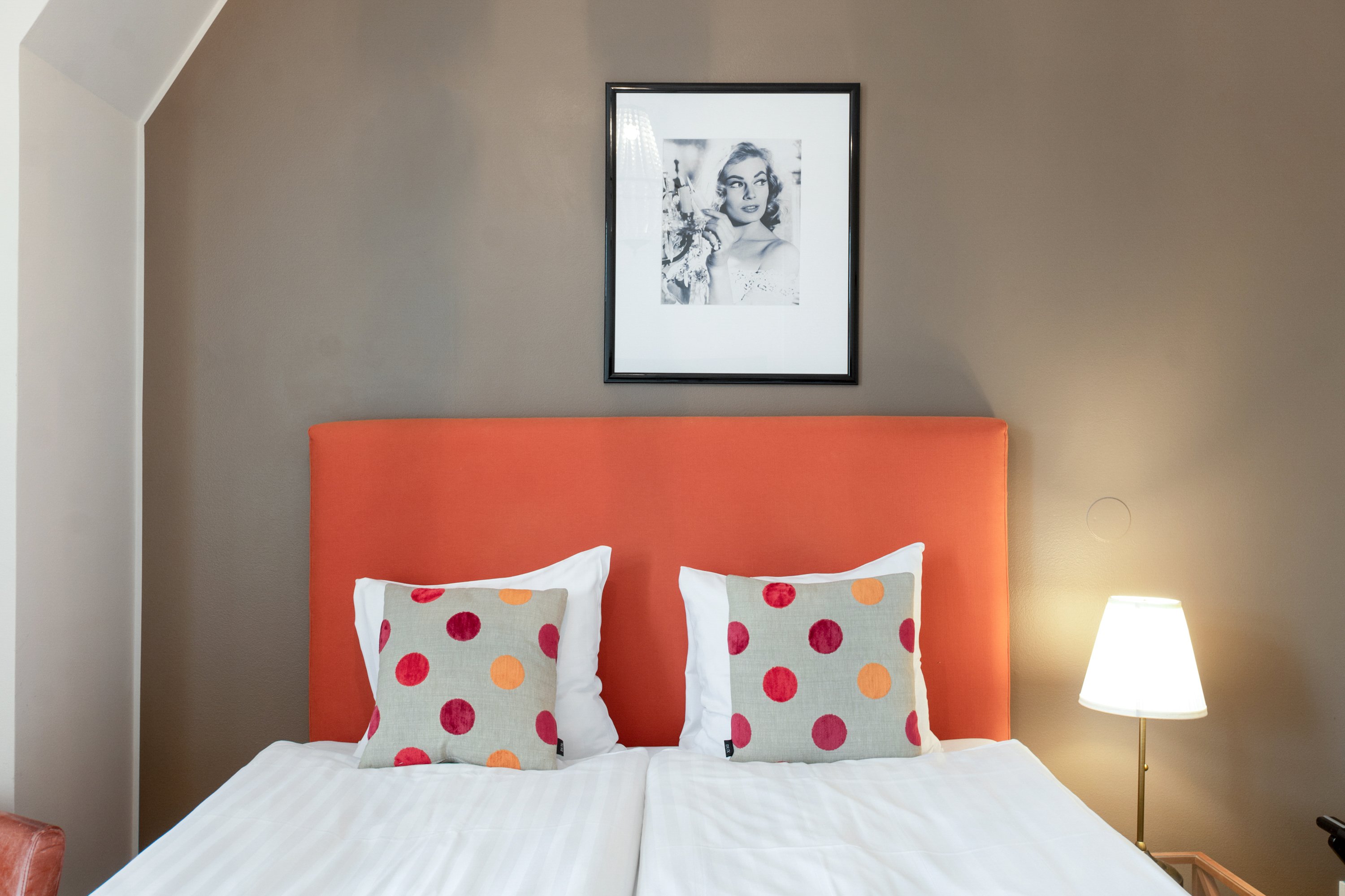 Hotellrum med säng, orange sänggavel och prickiga kuddar