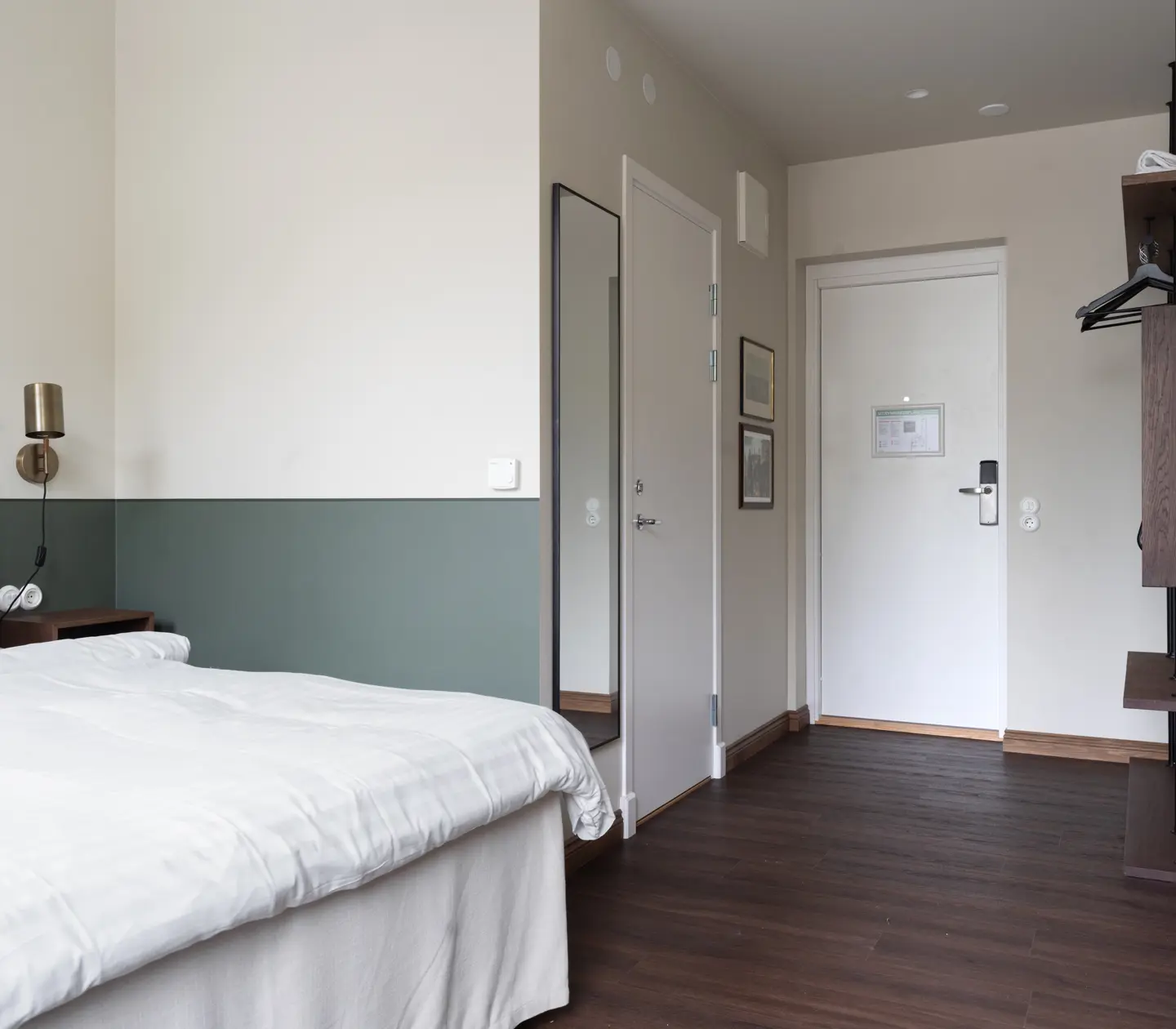 Ljust hotellrum med en dubbelsäng, träbord och stol, traditionell matta och konst på väggarna.