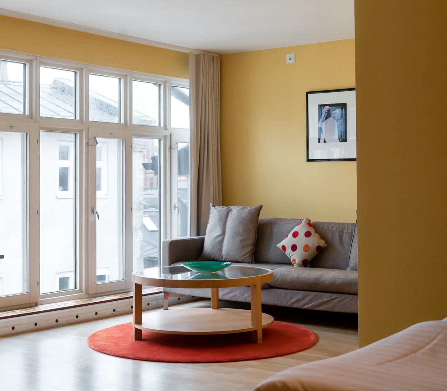 Yellow hotel room with gray sofa group, large windows and painting