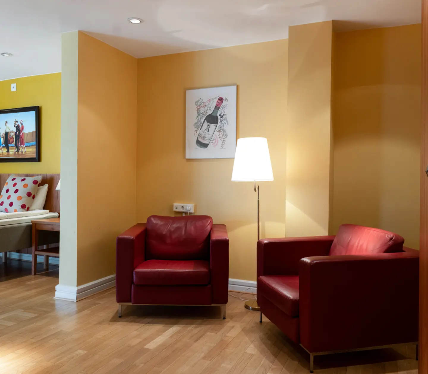 Yellow hotel room with bed, red leather armchairs and floor lamp