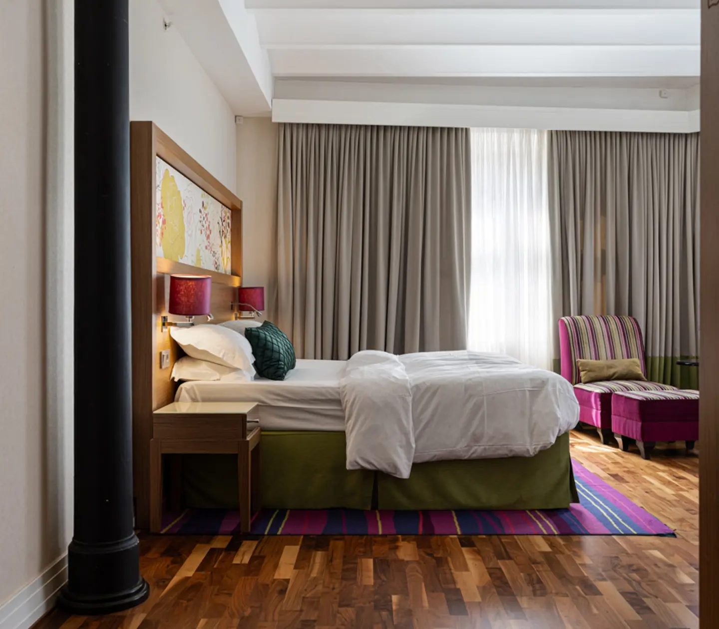 Hotellrum med dubbelsäng, fåtölj och stora fönster