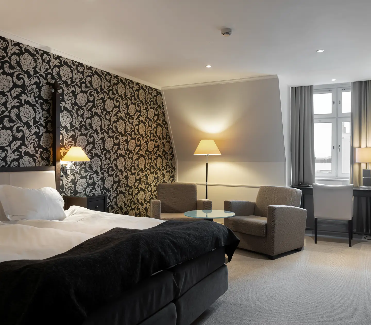 Nice hotel room with wallpaper, double bed, desk and armchairs
