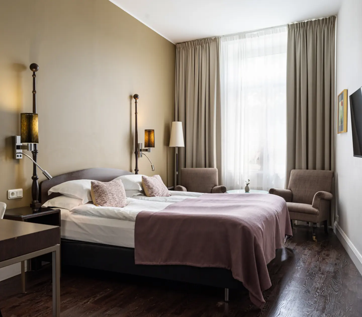 Bright hotel room with bed, purple armchairs and window