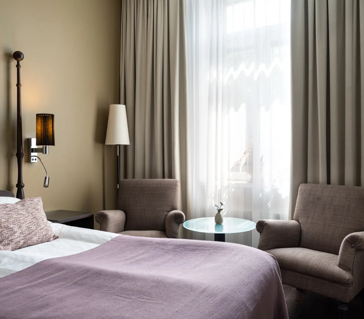 Bright hotel room with bed, purple armchairs and window