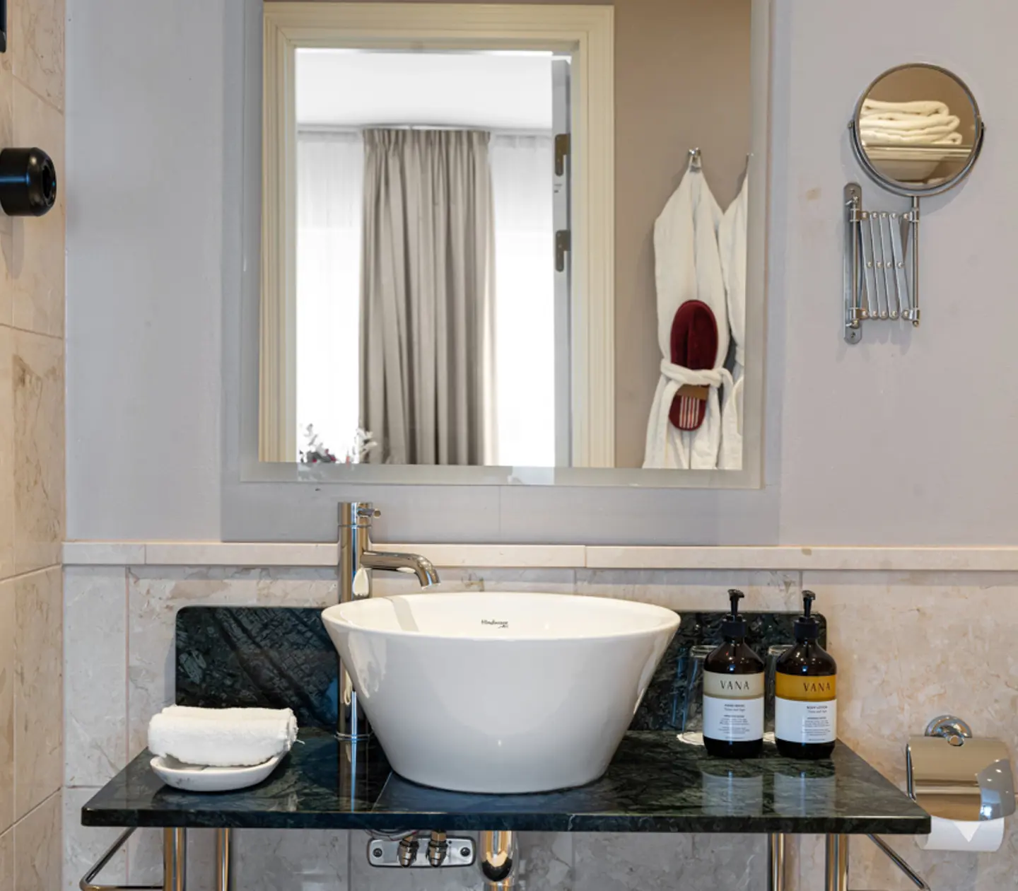 Elegant modern bathroom featuring a white vessel sink on a black marble countertop, complemented by luxury toiletries and neatly folded towels.
