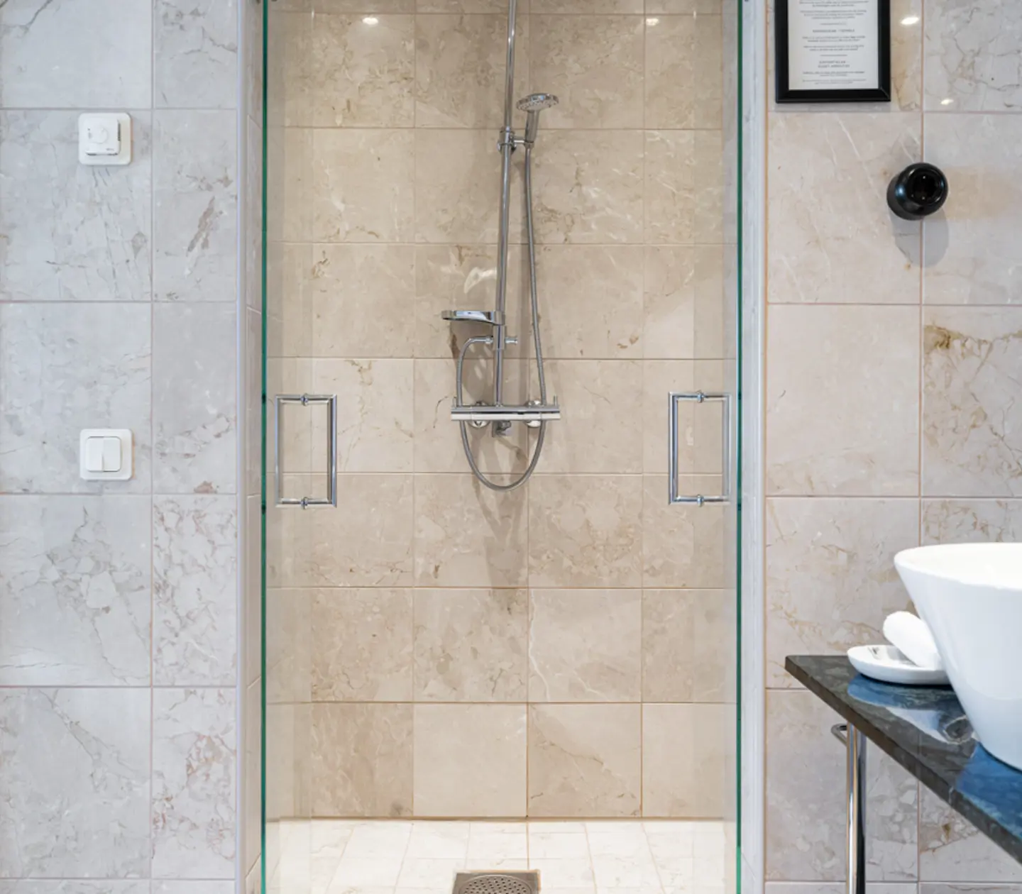Modern glass shower with marble tiles and chrome fixtures in a contemporary bathroom.