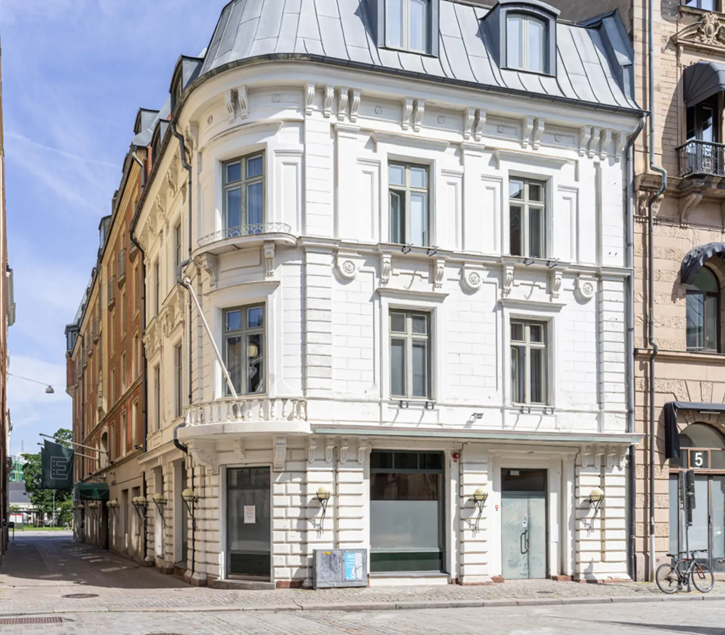 Historic European building on a sunny street corner, featuring classic architecture with ornate facade, arched windows, and decorative cornices, surrounded by urban landscape.