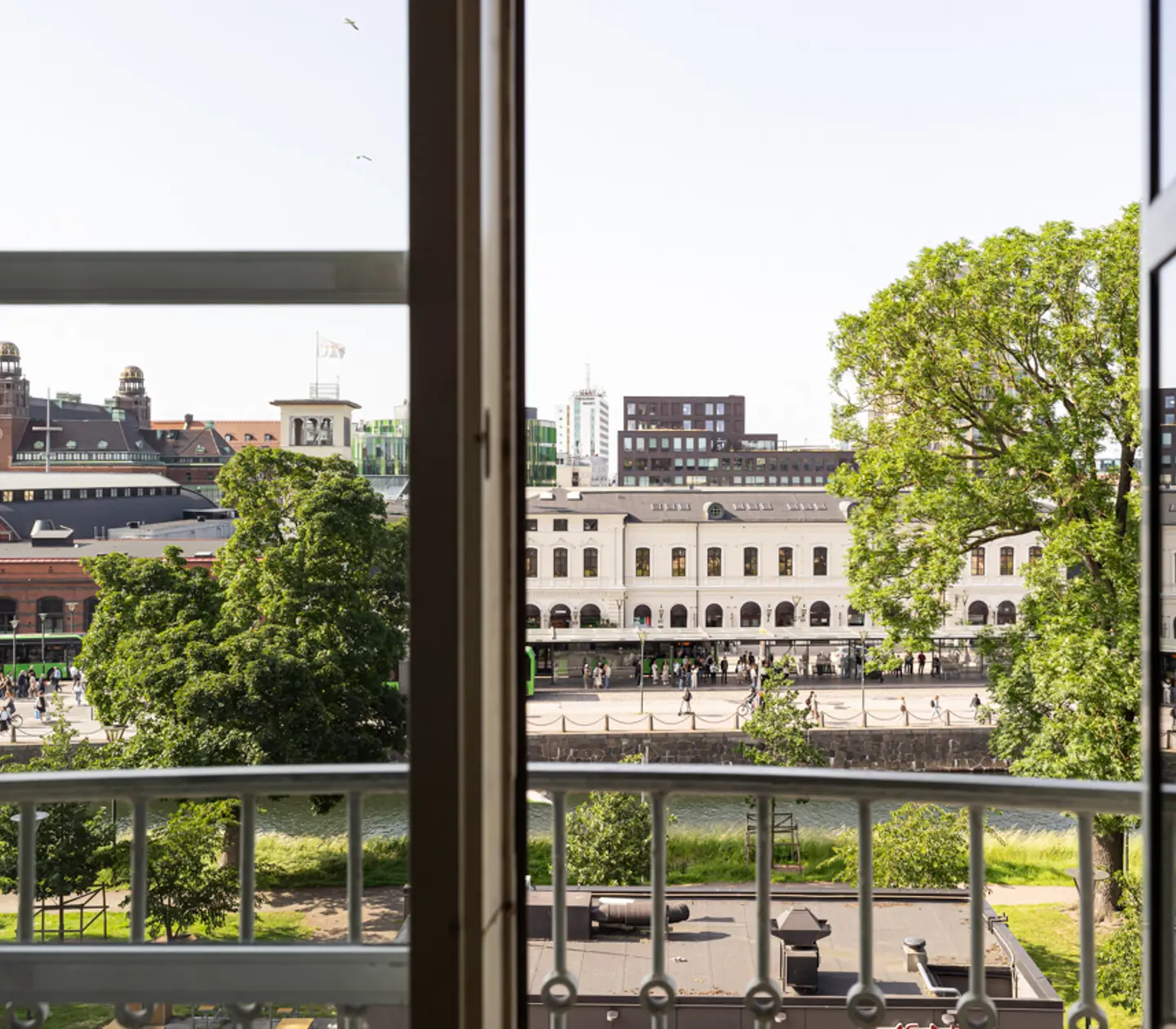 View from a window overlooking a historic European cityscape, featuring a large, white building, lush green trees, and a river in the foreground.