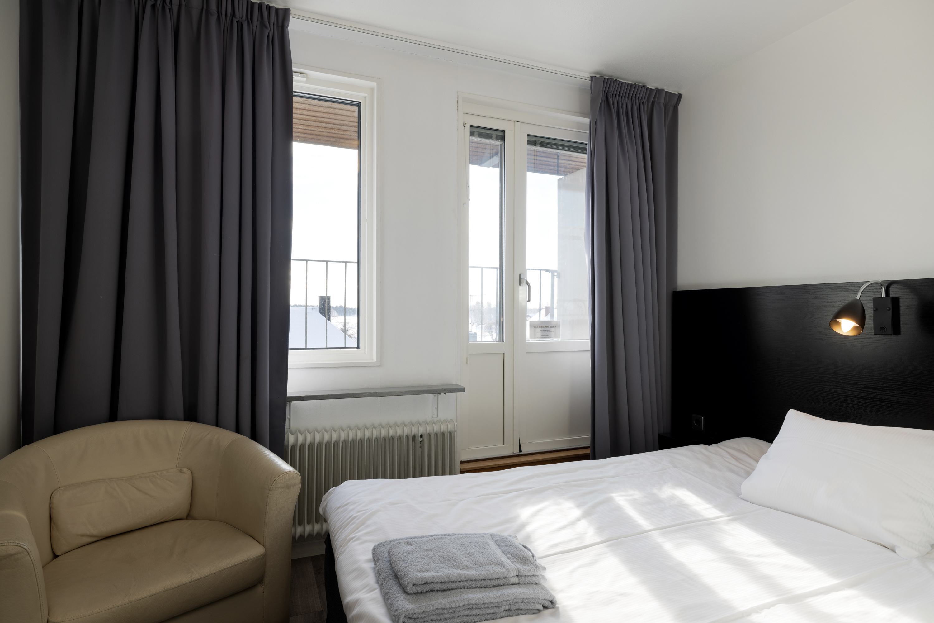 Hotellrum med säng, beige läderfåtölj och balkong