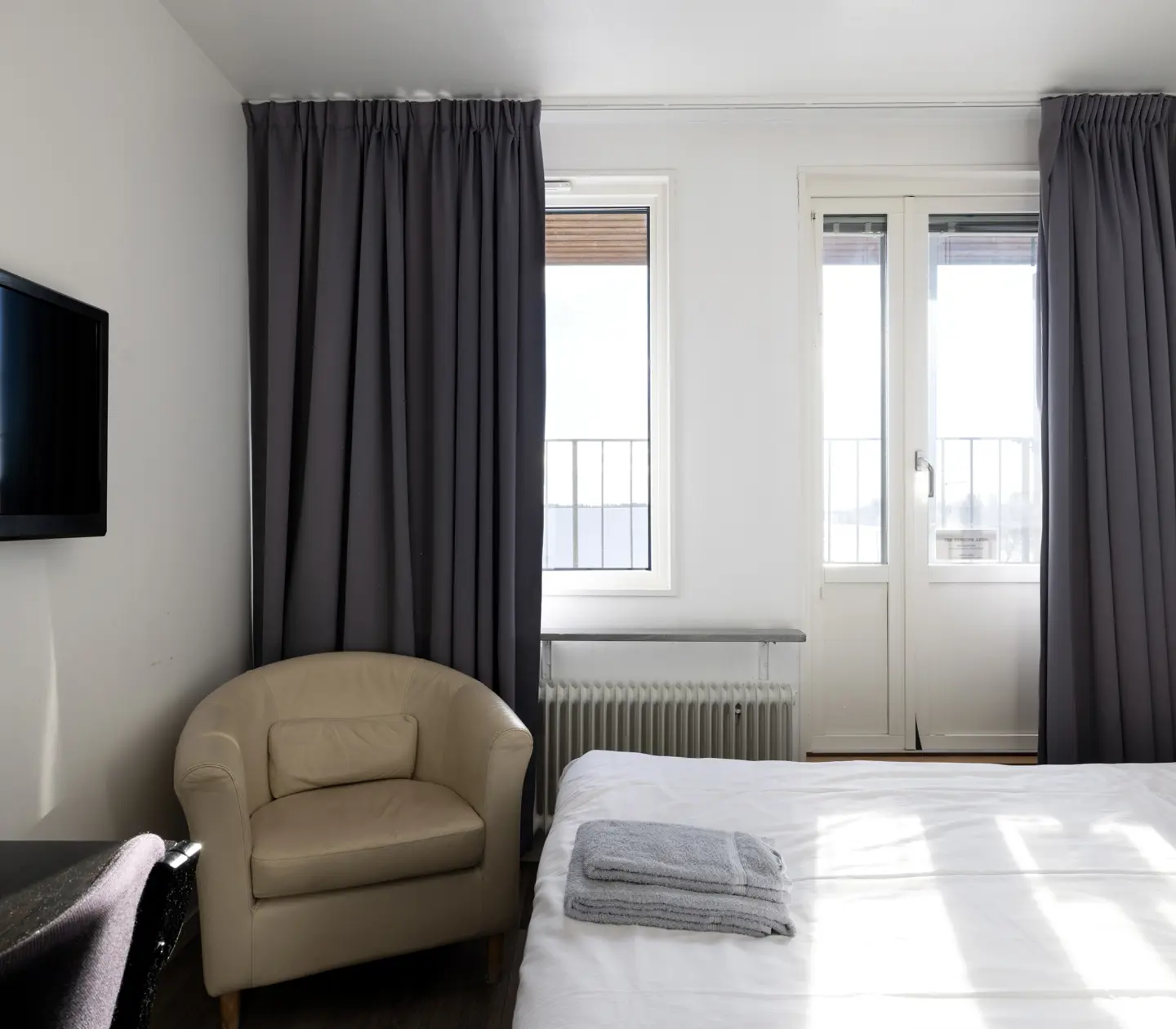 Hotel room with bed, beige leather armchair and TV
