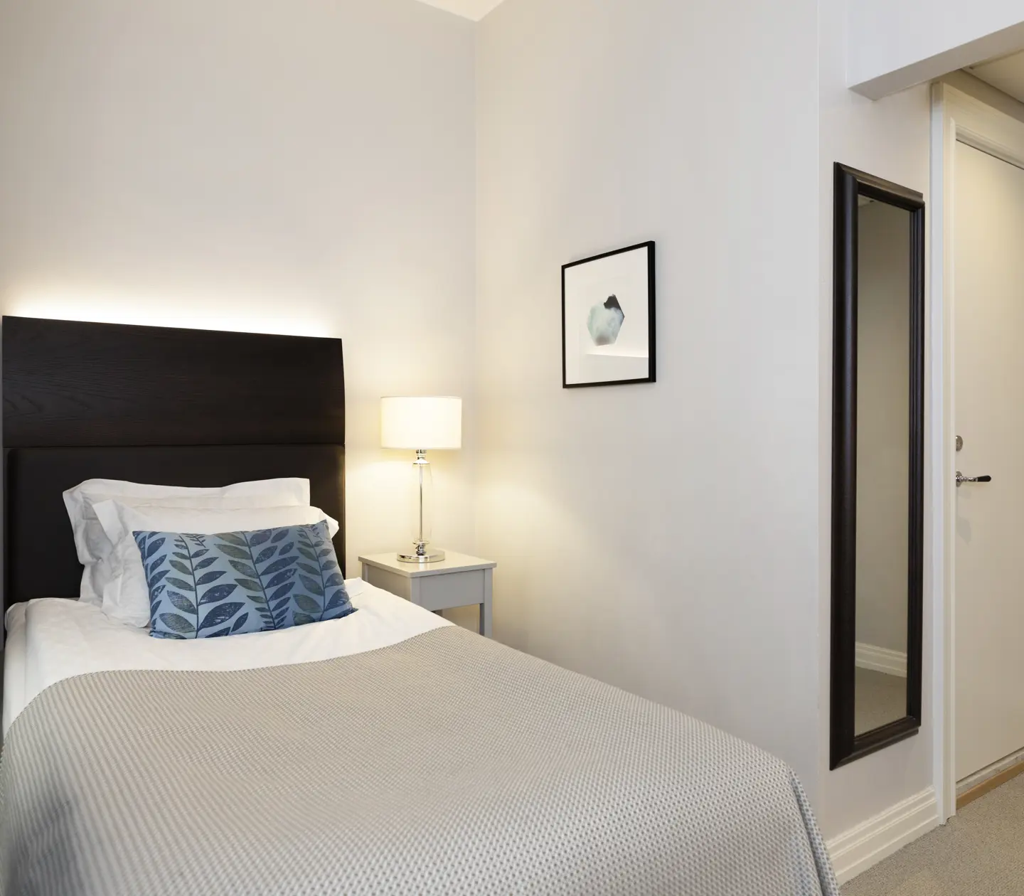 Bright hotel room with bed, bedside lamp and mirror
