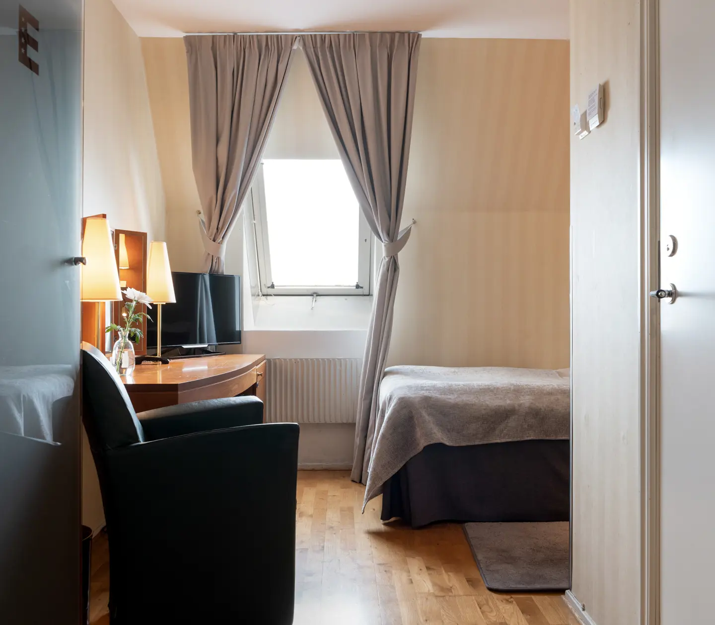 Bright hotel room with bed, slanted window and desk