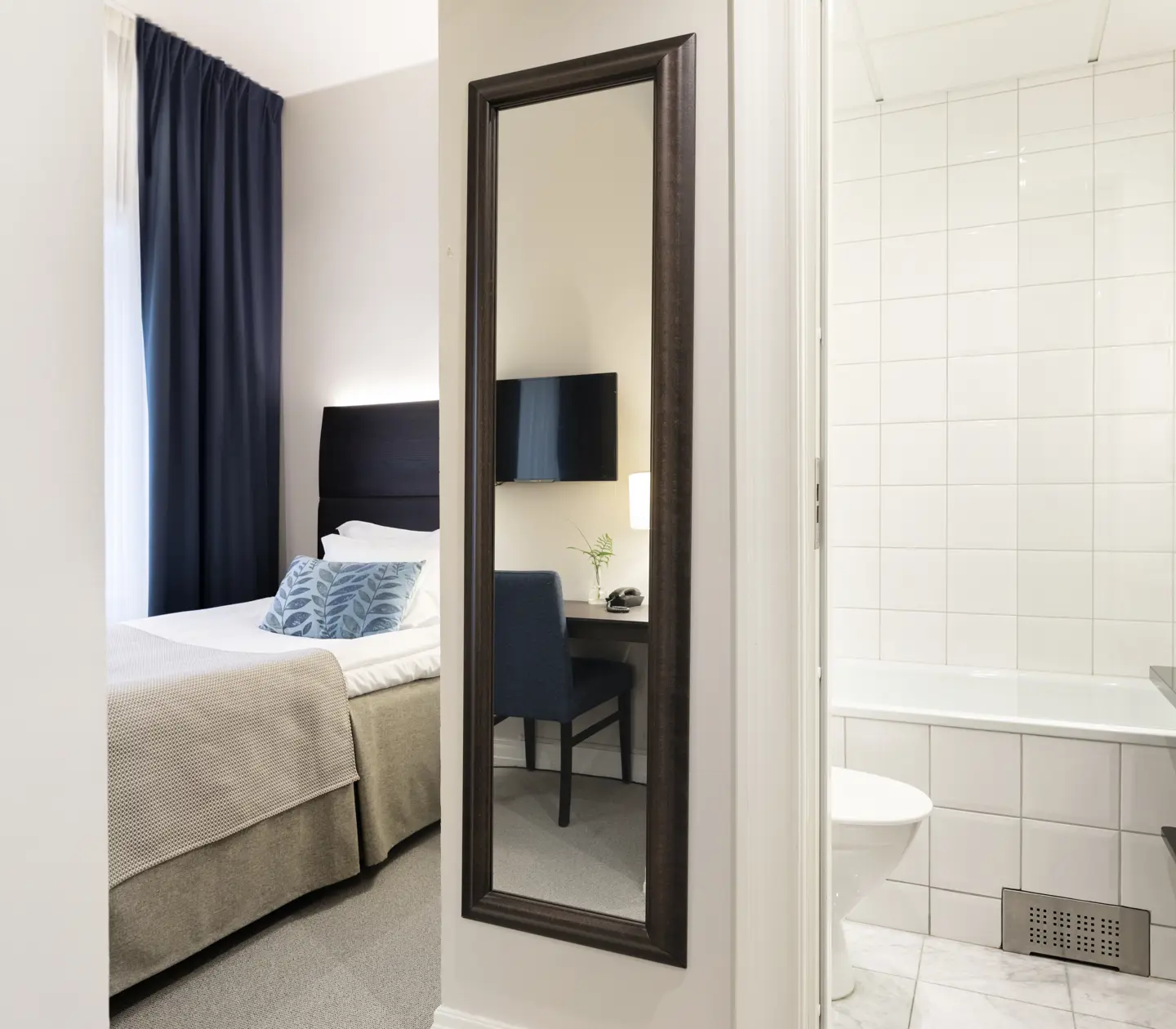 Bright hotel room with bed, door to bathroom and mirror
