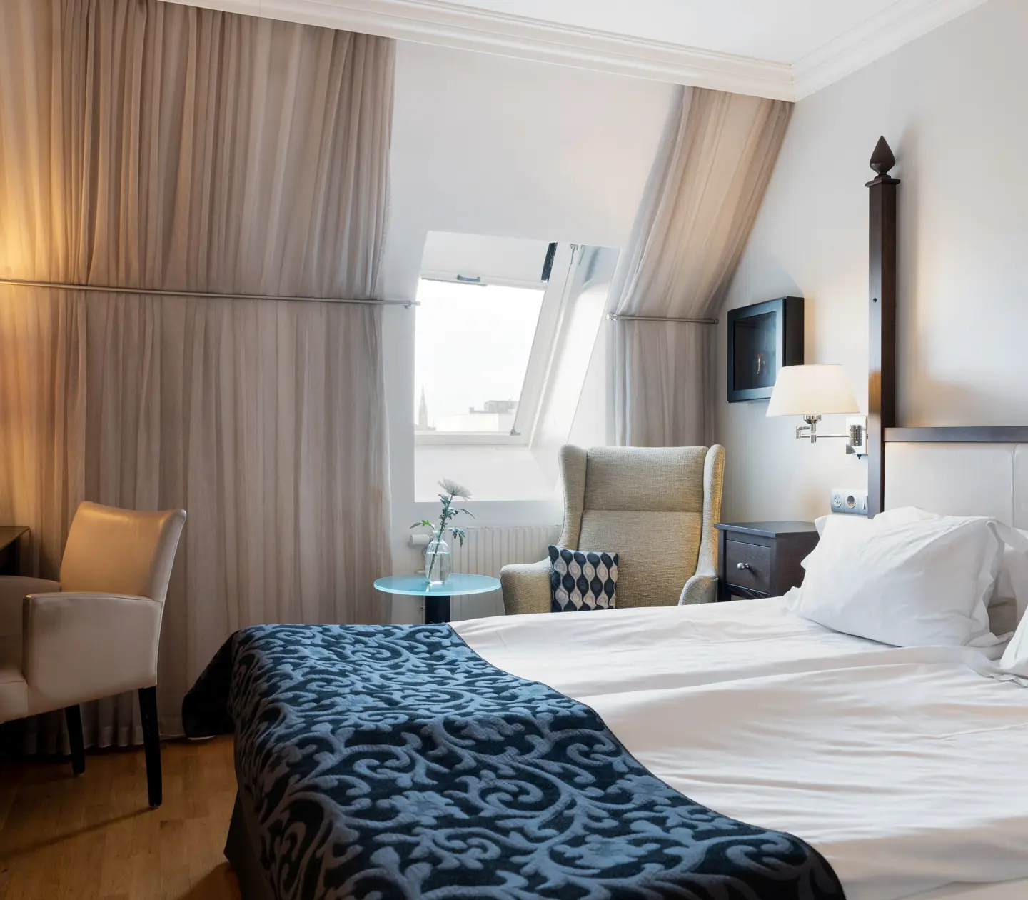 Bright hotel room with bed, desk and slanted ceiling