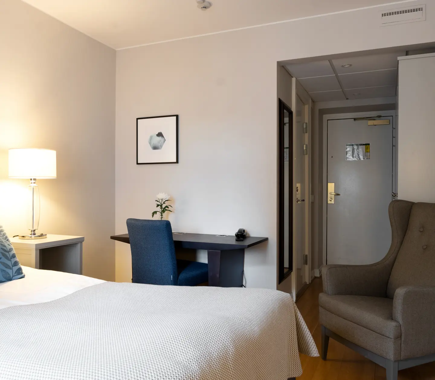 Bright hotel room with bed, armchair and desk