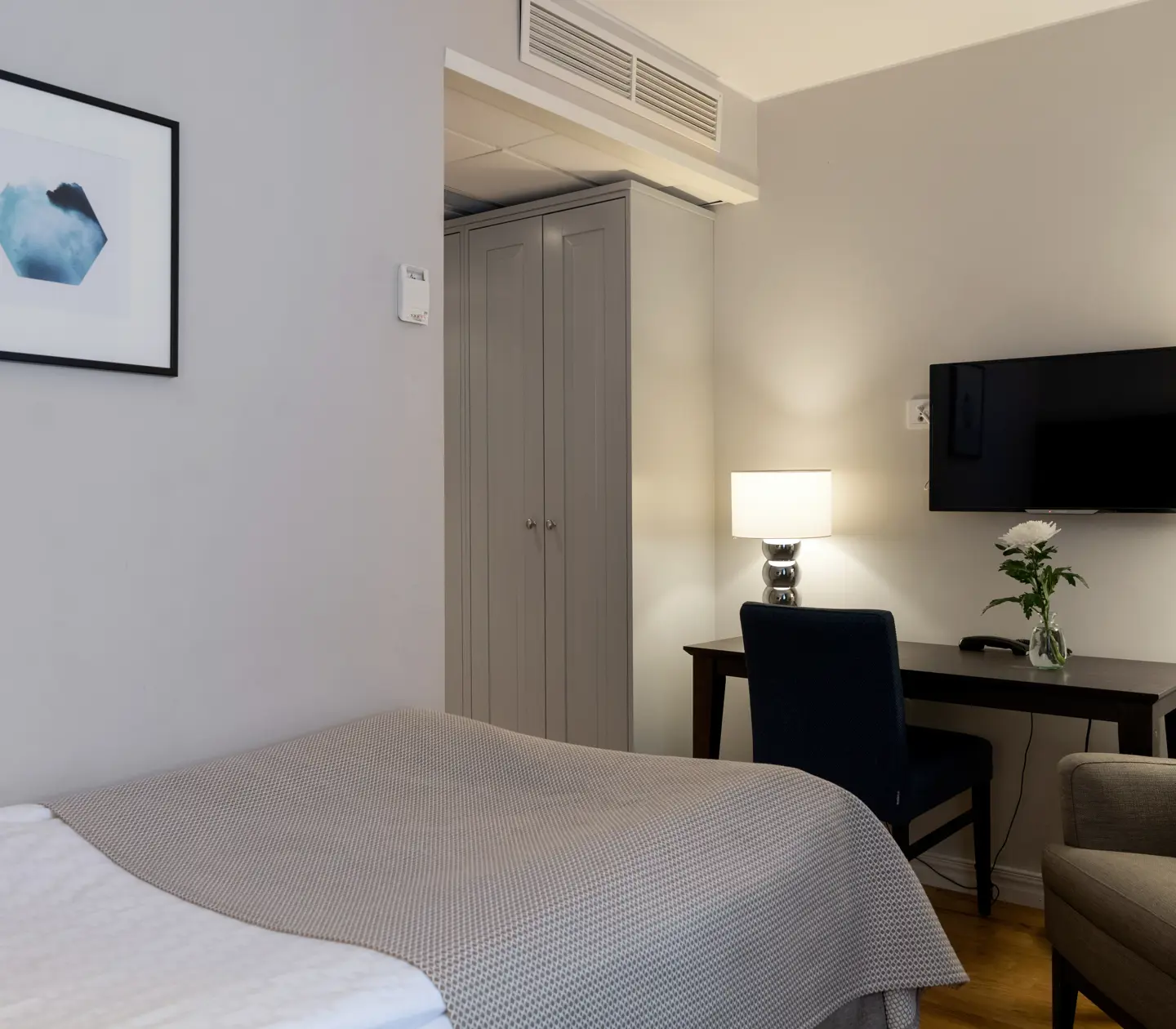 Bright hotel room with bed, desk and armchair